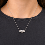 A person wearing a dark, ribbed sweater and the Bezel Set East-West Lozenge Diamond Pendant Necklace in white gold—an 18K chain with a geometric pendant set with F color diamonds and small gemstones.