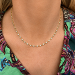 A close-up of a person wearing the Chasing Pears Diamond Garland Necklace, featuring 18K gold and pear-shaped diamonds, paired with a vibrant green, purple, and pink patterned top.