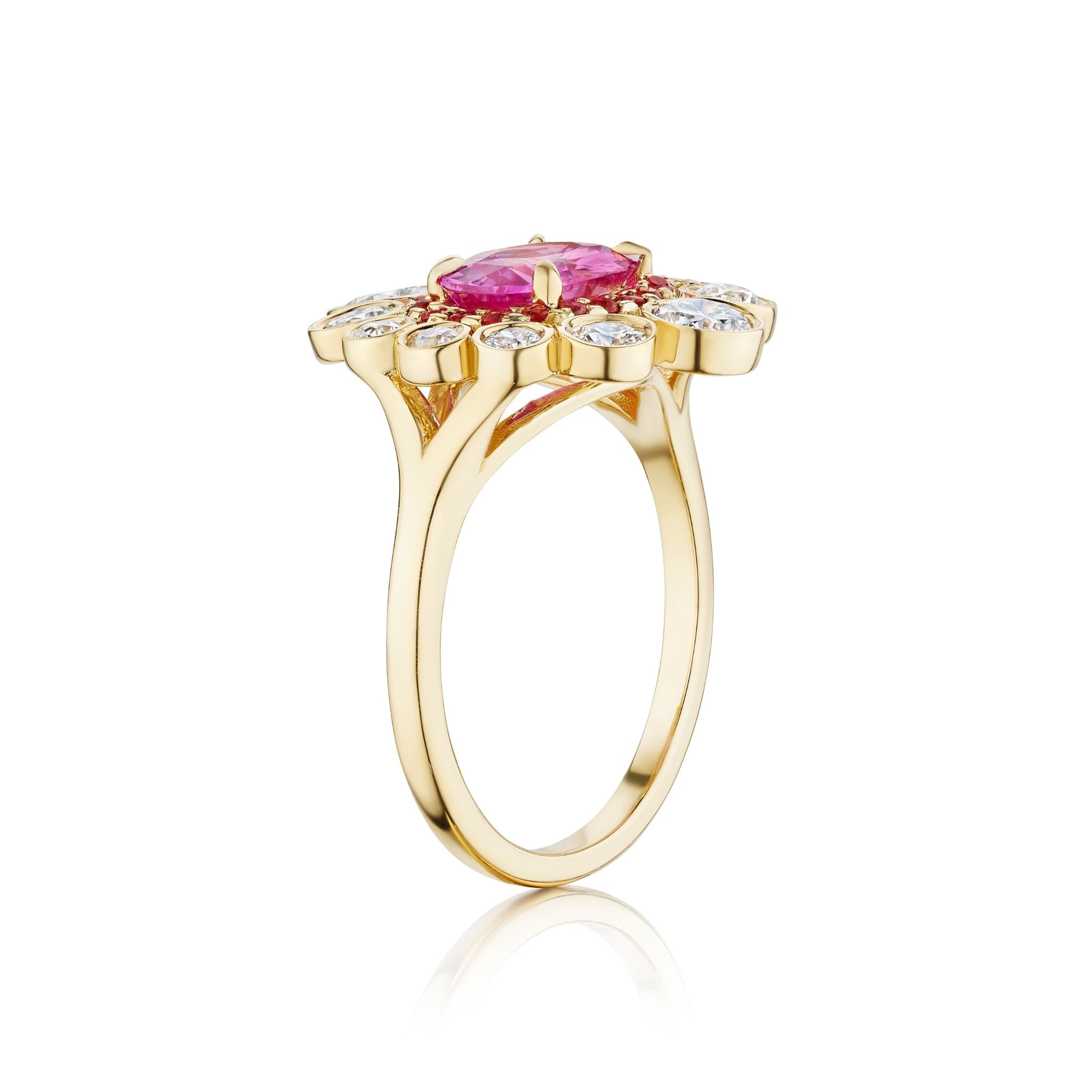 The Cocktail Ring in Yellow Gold features an east-west set oval pink sapphire at the center, surrounded by round diamonds in a floral halo design, shown from a side angle on a plain white background.