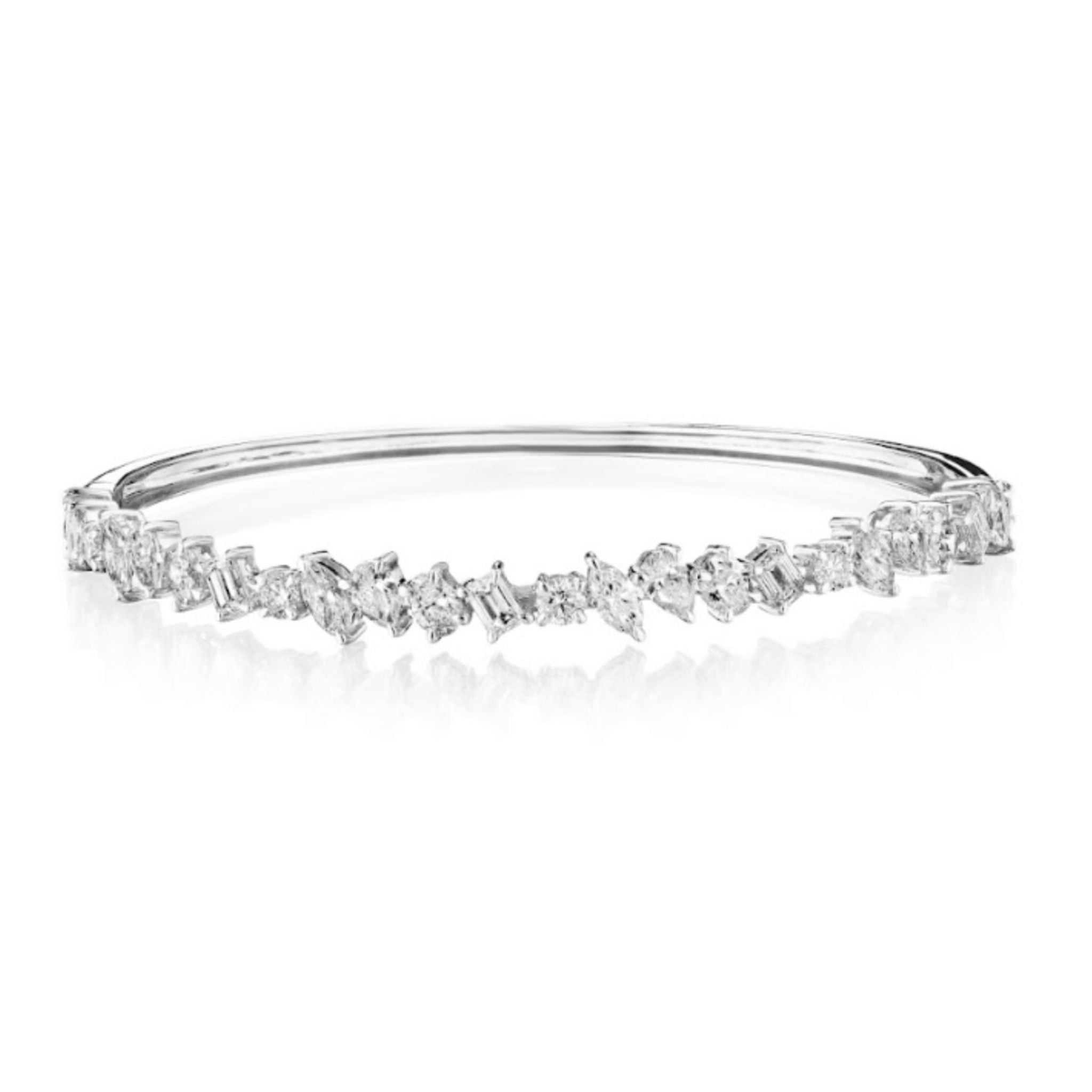 The Marching Mixed Shape Diamond Bangle is a silver bracelet adorned with an array of sparkling, mixed-shape clear gemstones—including exquisite emerald cut VS clarity diamonds—set along the upper half, and shown against a white background.