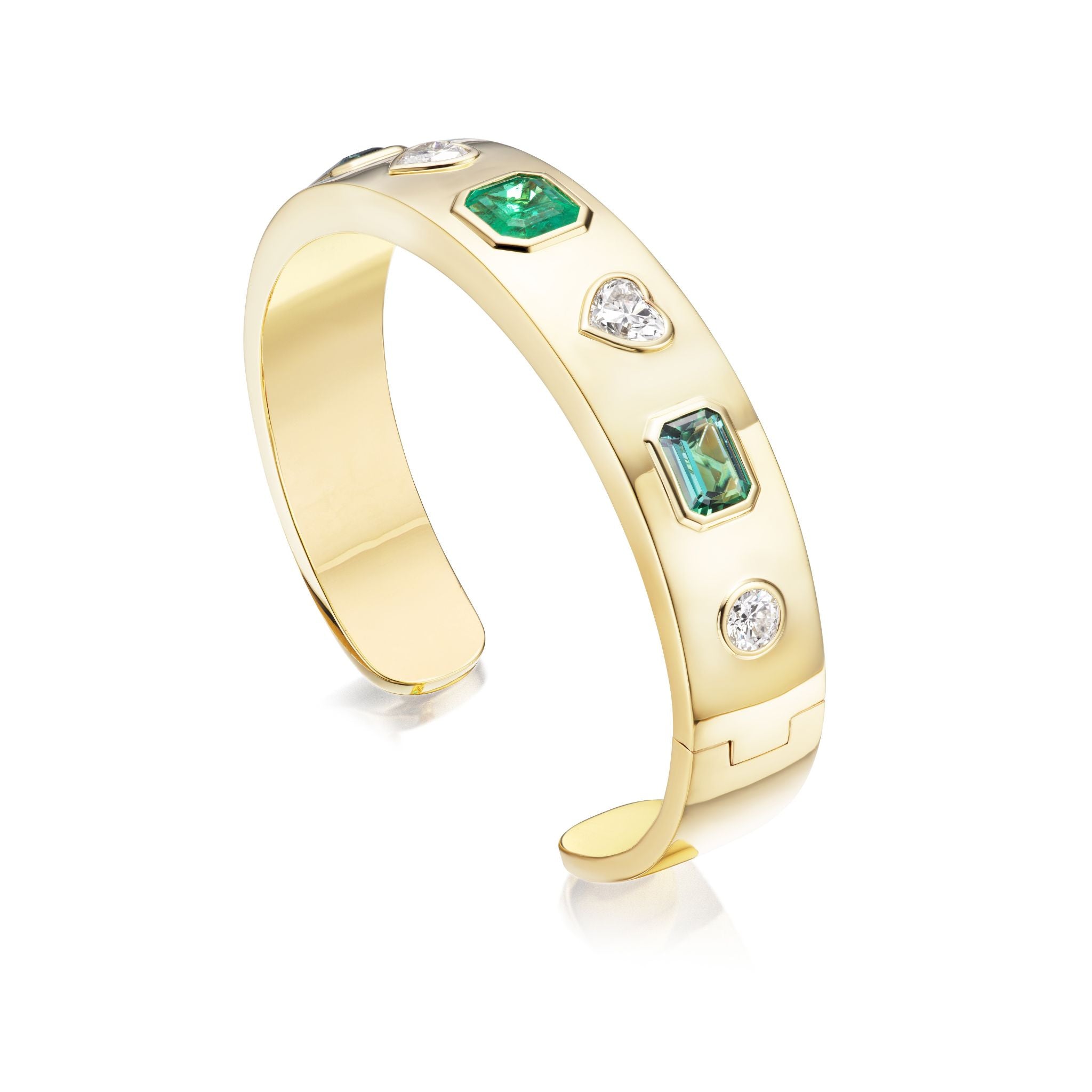 The Bezel Set Mixed Shape Diamond and Emerald Bangle in Yellow Gold showcases 18K yellow gold adorned with bezel-set green emeralds and clear diamonds in various shapes, including heart-shaped diamonds and emerald-cut emeralds, all set along its polished band and displayed against a white background.