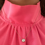 A close-up of a person wearing a pink high-neck blouse with the Cushion Cut Diamond Collet Pendant in Yellow and Blackened Gold, featuring a round, sparkling cushion cut diamond.