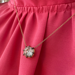 The Cushion Cut Diamond Collet Pendant in Yellow and Blackened Gold rests against pink, pleated fabric, its large cushion cut diamond set in vibrant gold for a striking look.