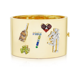 The Custom Designed Gemstone Charm Cuff in Yellow Gold showcases colorful charms—a champagne bottle, two hearts, the number 7, a flower bouquet, and a couple embracing—on an elegant wide gold bracelet.