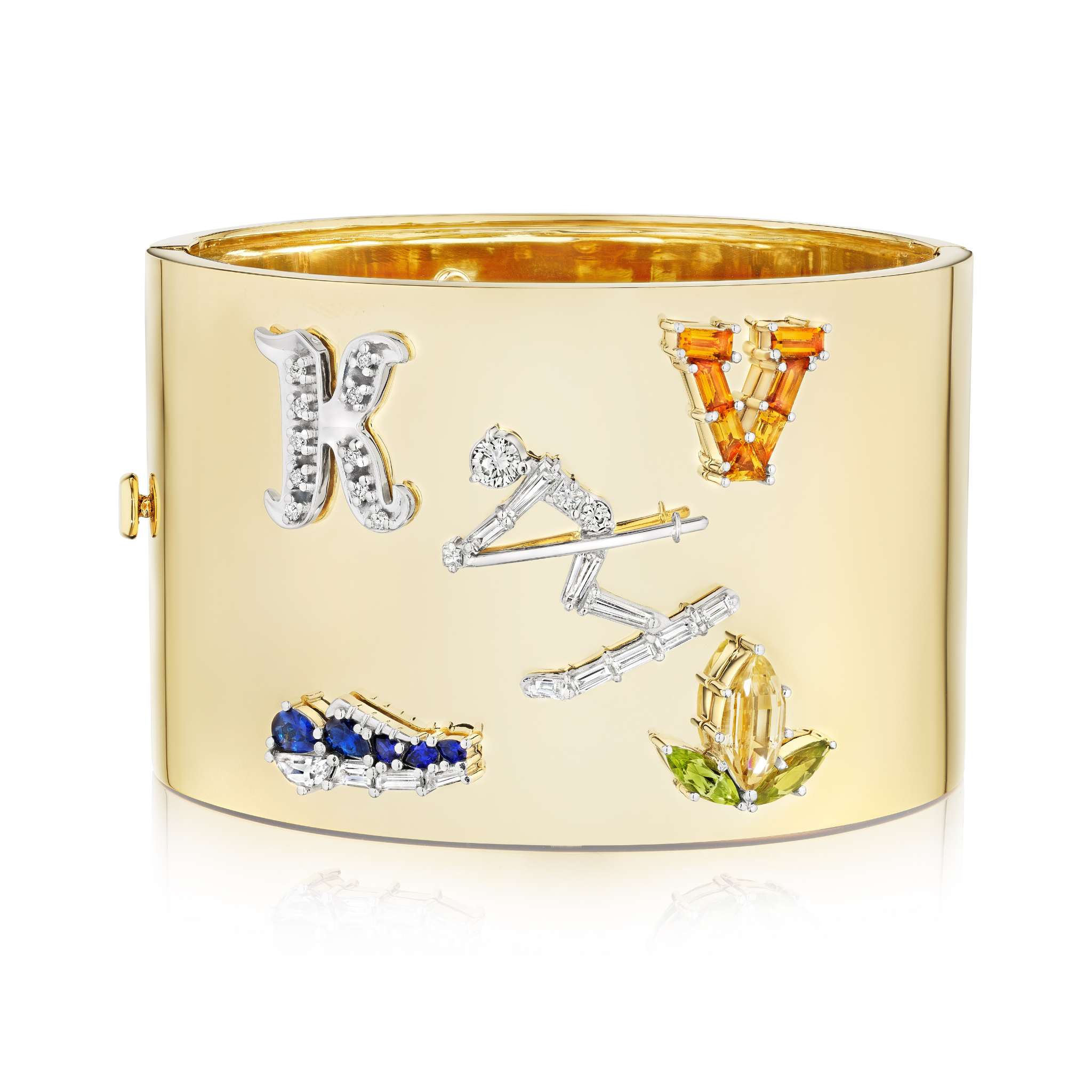 The Custom Designed Gemstone Charm Cuff in Yellow Gold features a wide, polished band with jeweled K and V letters, a gemstone line, angular shapes, and clusters of yellow-green and blue gemstones.