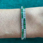 The Emerald and Diamond Bracelet, measuring 7 inches and featuring alternating green emeralds and clear diamonds, is displayed on a wrist against teal fabric.