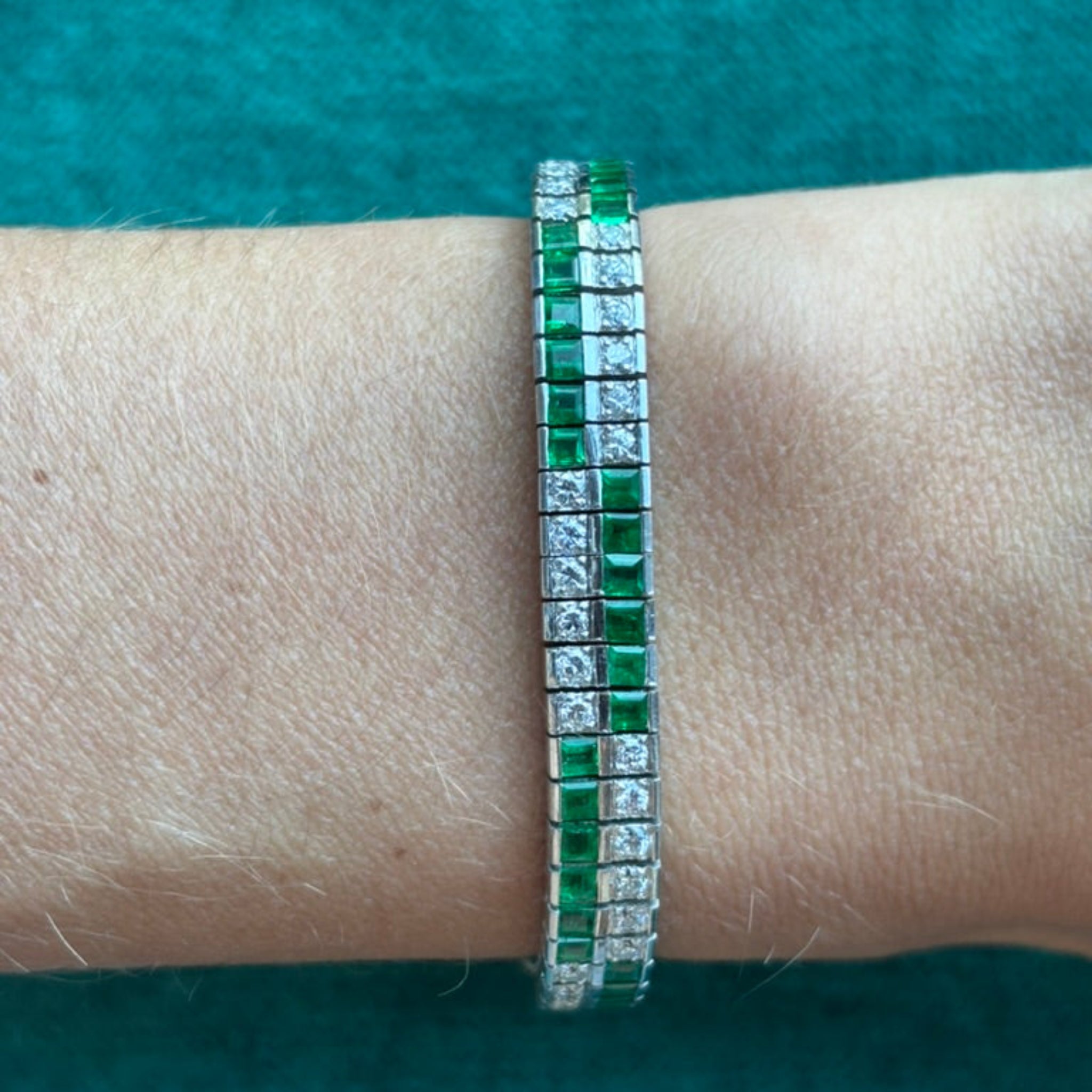 The Emerald and Diamond Bracelet, measuring 7 inches and featuring alternating green emeralds and clear diamonds, is displayed on a wrist against teal fabric.