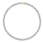 The Collet Set Oval Diamond Tennis Necklace in Black Rhodium showcases a continuous loop of oval diamonds, each gracefully set in silver-toned metal with refined black rhodium plating and highlighted by a single round 18k yellow gold clasp at the top center. Displayed against a white background.