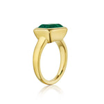 An East-West Bezel Set Emerald Cut Emerald Engagement Ring in Yellow Gold features a large, faceted emerald-cut emerald set in a modern geometric bezel atop an 18K yellow gold band, displayed on a white background.