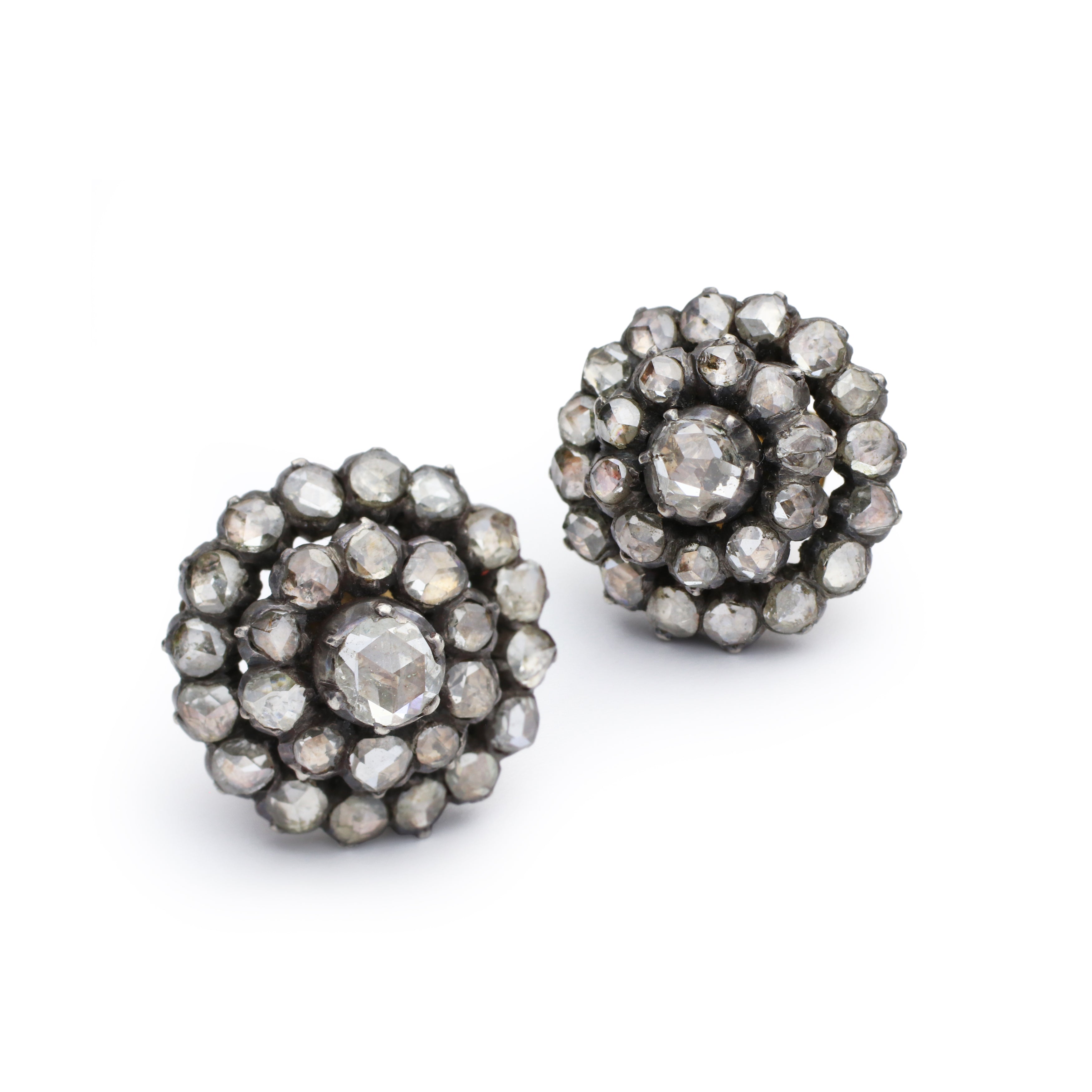 The Diamond Cluster Earrings, circa 1880, showcase clusters of faceted gemstones and rose-cut diamonds arranged in a layered floral motif on a silver and gold-toned metal base, displayed against a white background.