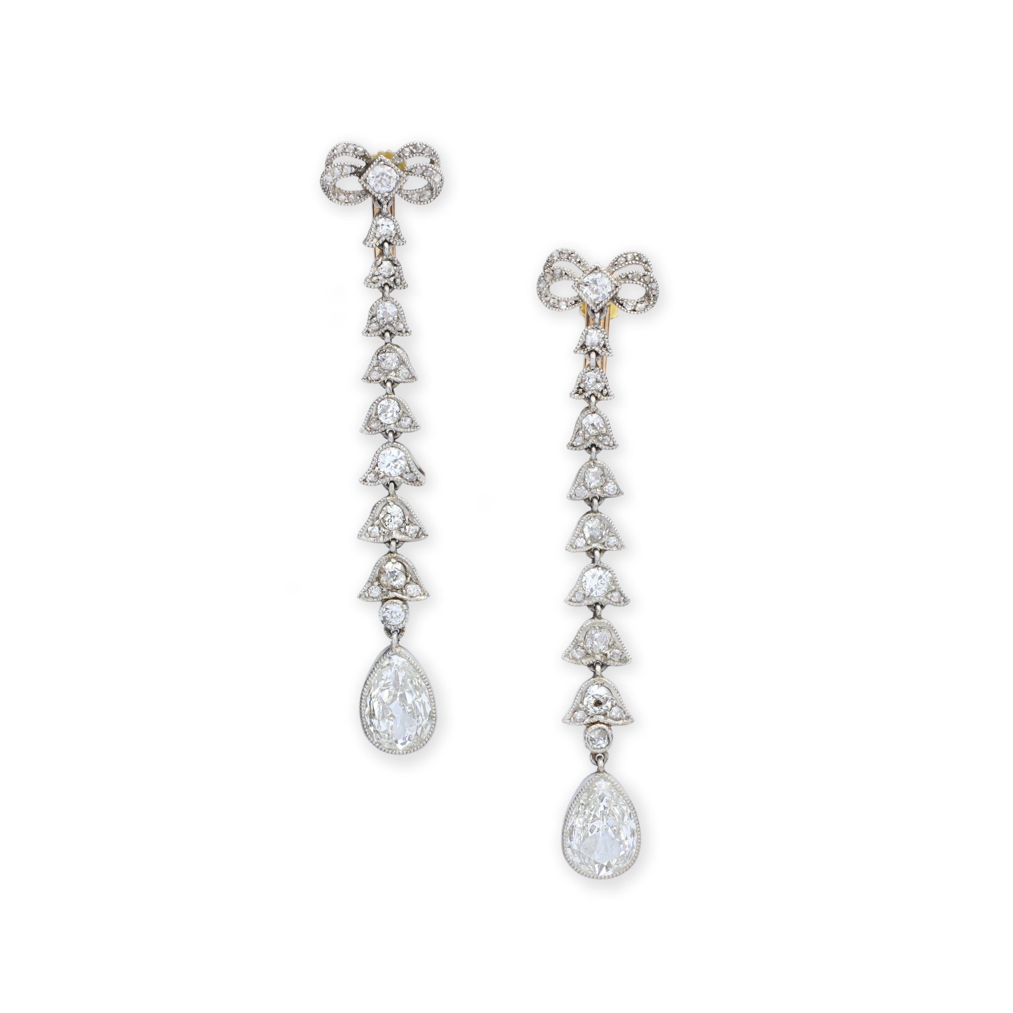 Antique Diamond Earrings featuring graceful bow-shaped tops, a vertical row of sparkling diamonds, and a prominent teardrop diamond at the base, all beautifully set in platinum and white gold metal from circa 1910.