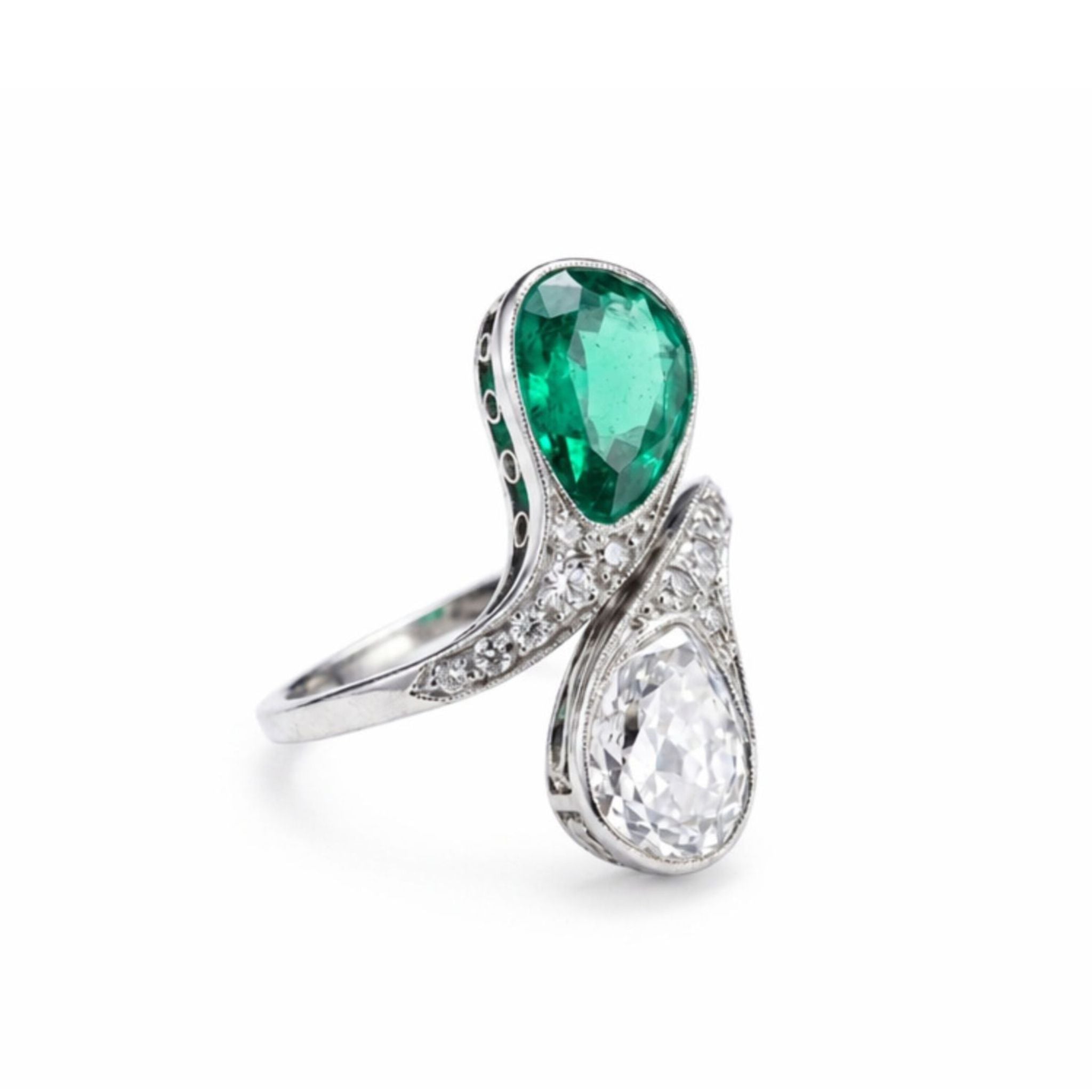 The Early 20th Century Emerald And Diamond Bypass Ring features a platinum band with a pear-shaped Colombian emerald and a pear-shaped diamond set opposite each other, accented by small round diamonds.