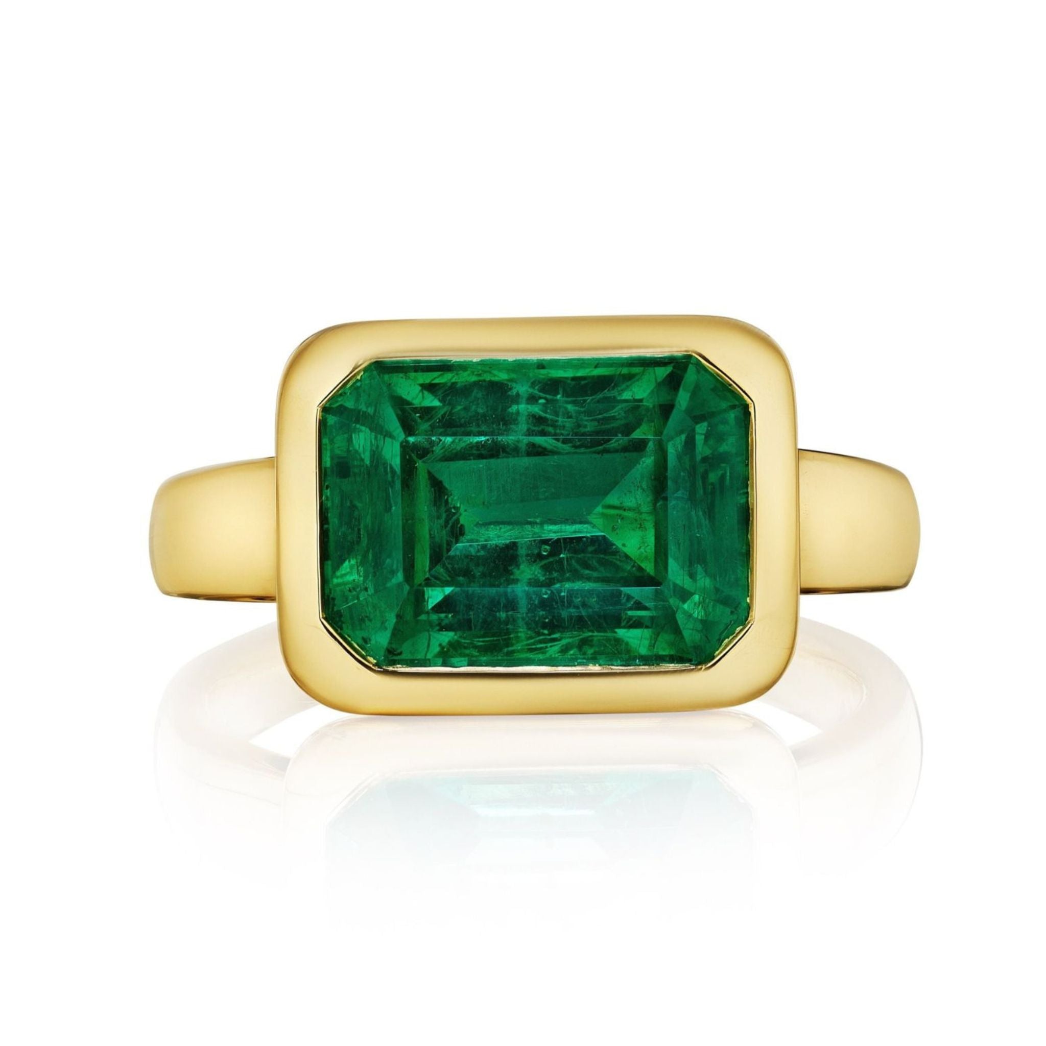 The East-West Bezel Set Emerald Cut Emerald Engagement Ring in Yellow Gold features an emerald cut emerald in a rectangular bezel on a sleek 18K gold band, shown against a white background.