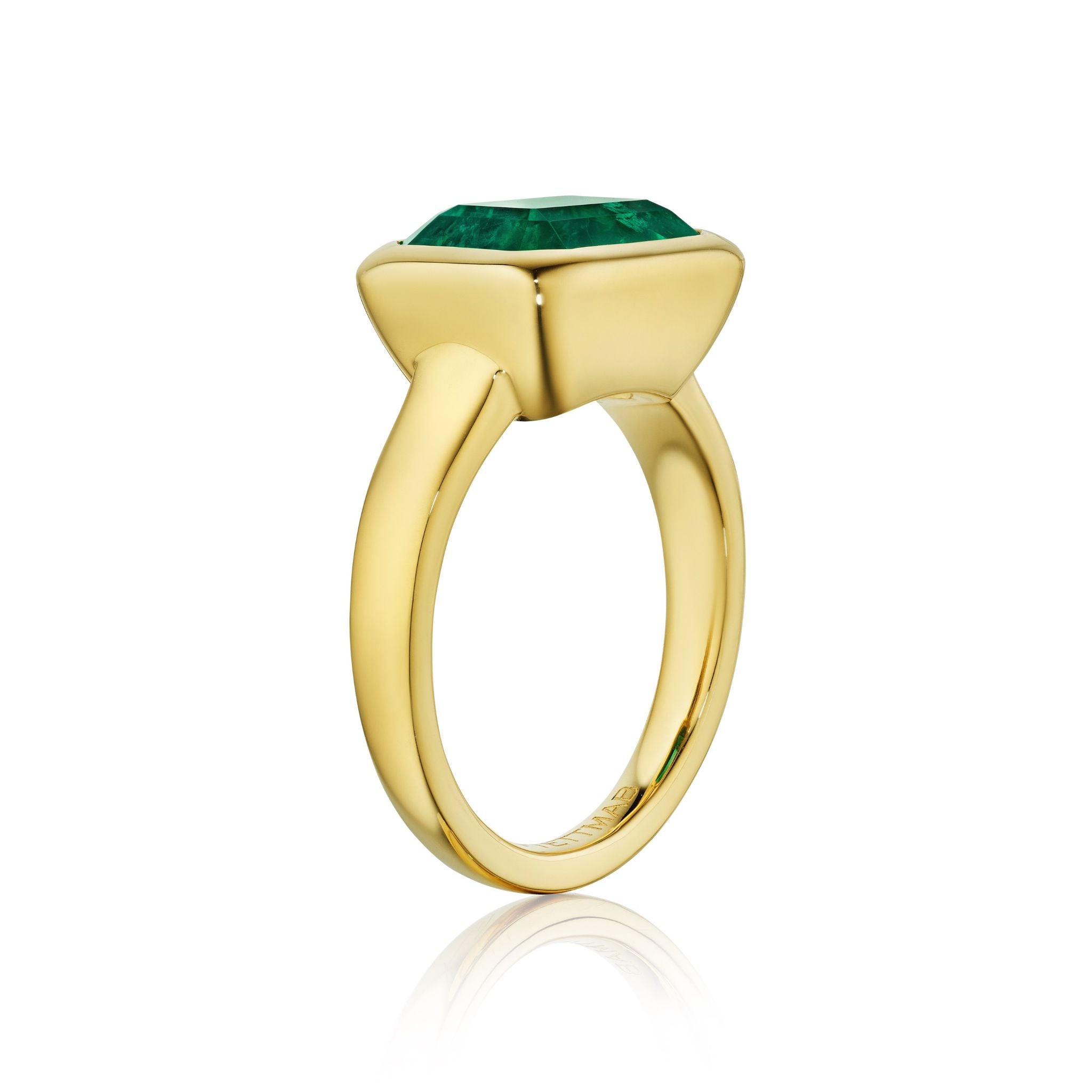 The East-West Bezel Set Emerald Cut Emerald Engagement Ring in Yellow Gold features a large emerald cut emerald in a modern bezel setting on a sleek gold band, shown against a white background.