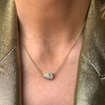A close-up of a person wearing the East-West Bezel Set Pear Diamond Pendant in Yellow Gold on a 16-inch chain, paired with a shiny gold blazer.
