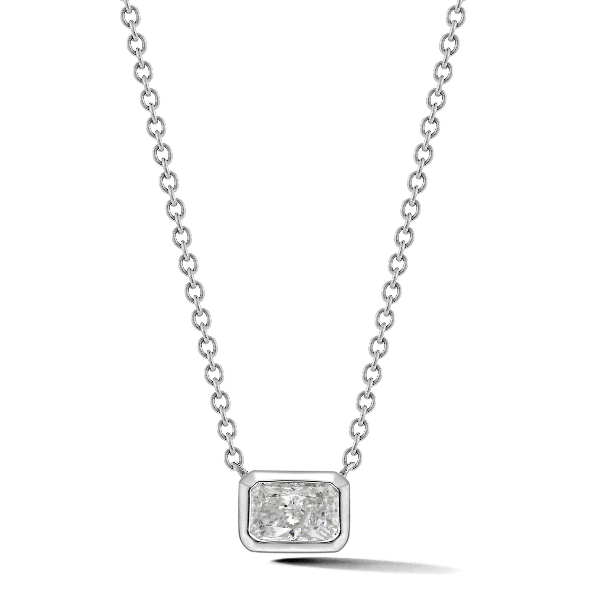 The East-West Bezel Set Radiant Cut Diamond Solitaire Pendant in White Gold showcases a radiant cut diamond in a rectangular, bezel setting on an 18K white gold chain, displayed against a white background.