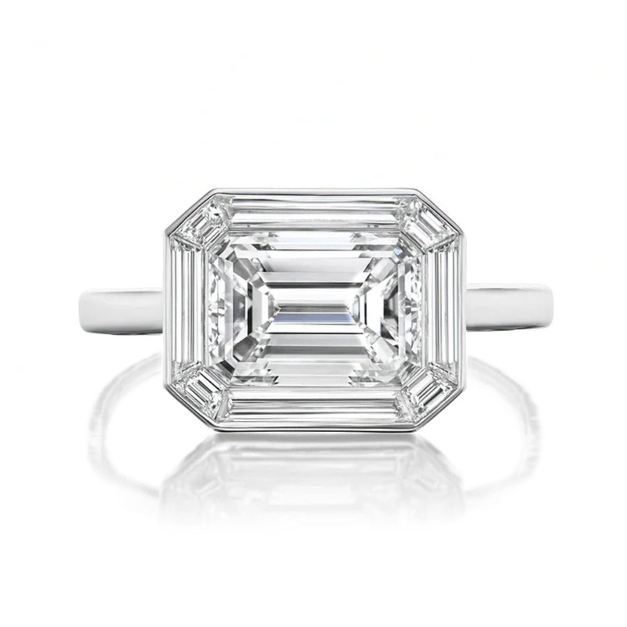 A close-up of the East-West Set Mosaic Diamond Engagement Ring, showcasing a large emerald-cut diamond with tapered corners and a baguette halo, set in polished white gold against a white background.
