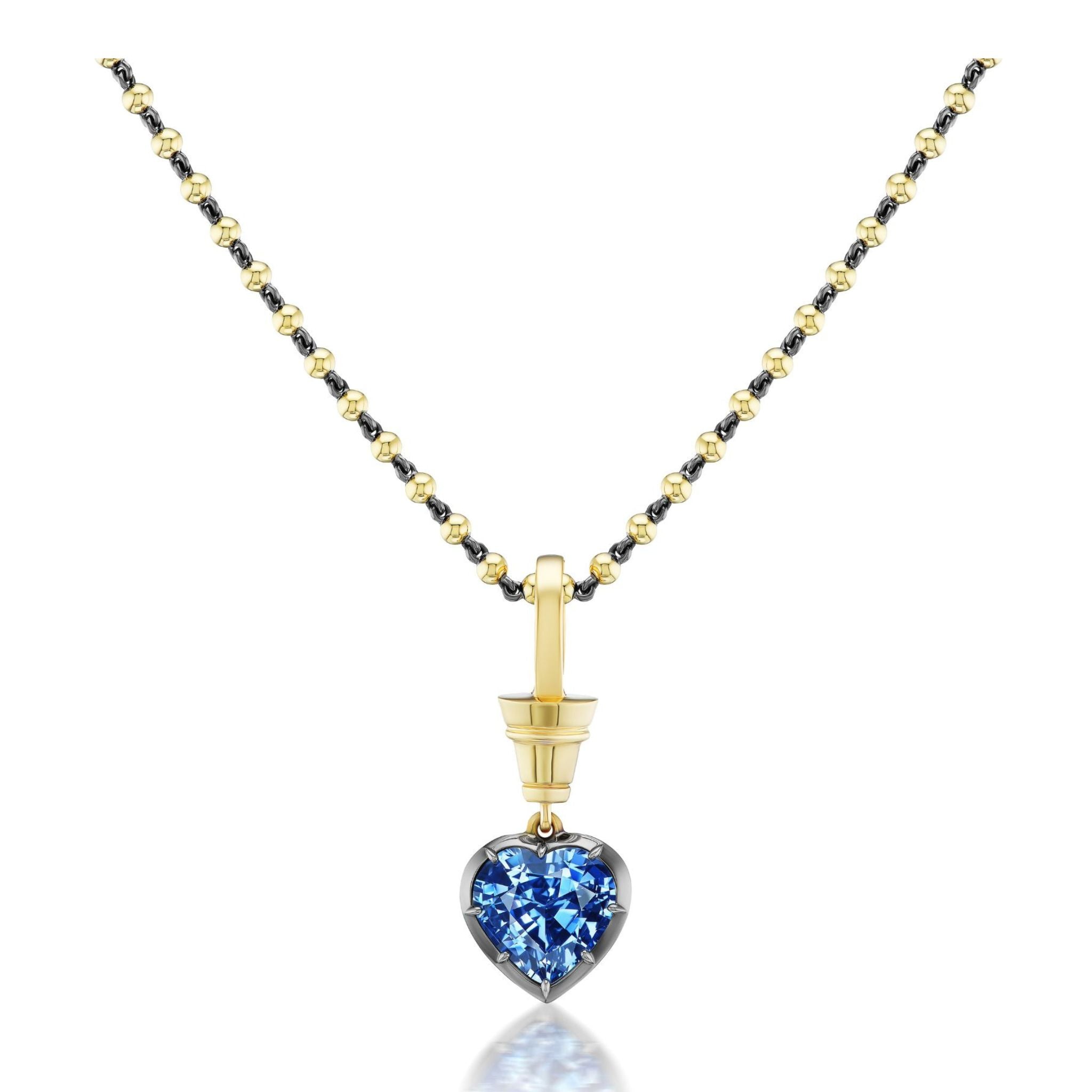 Collet Set Heart Shape Blue Sapphire Necklace in Black Rhodium and Yellow Gold showcases alternating gold and black rhodium beads, highlighted by a yellow gold pendant that holds a captivating heart shape blue sapphire. The faceted gemstone dazzles on a plain white backdrop, elegantly enhanced by the luxurious 18k yellow gold accents.