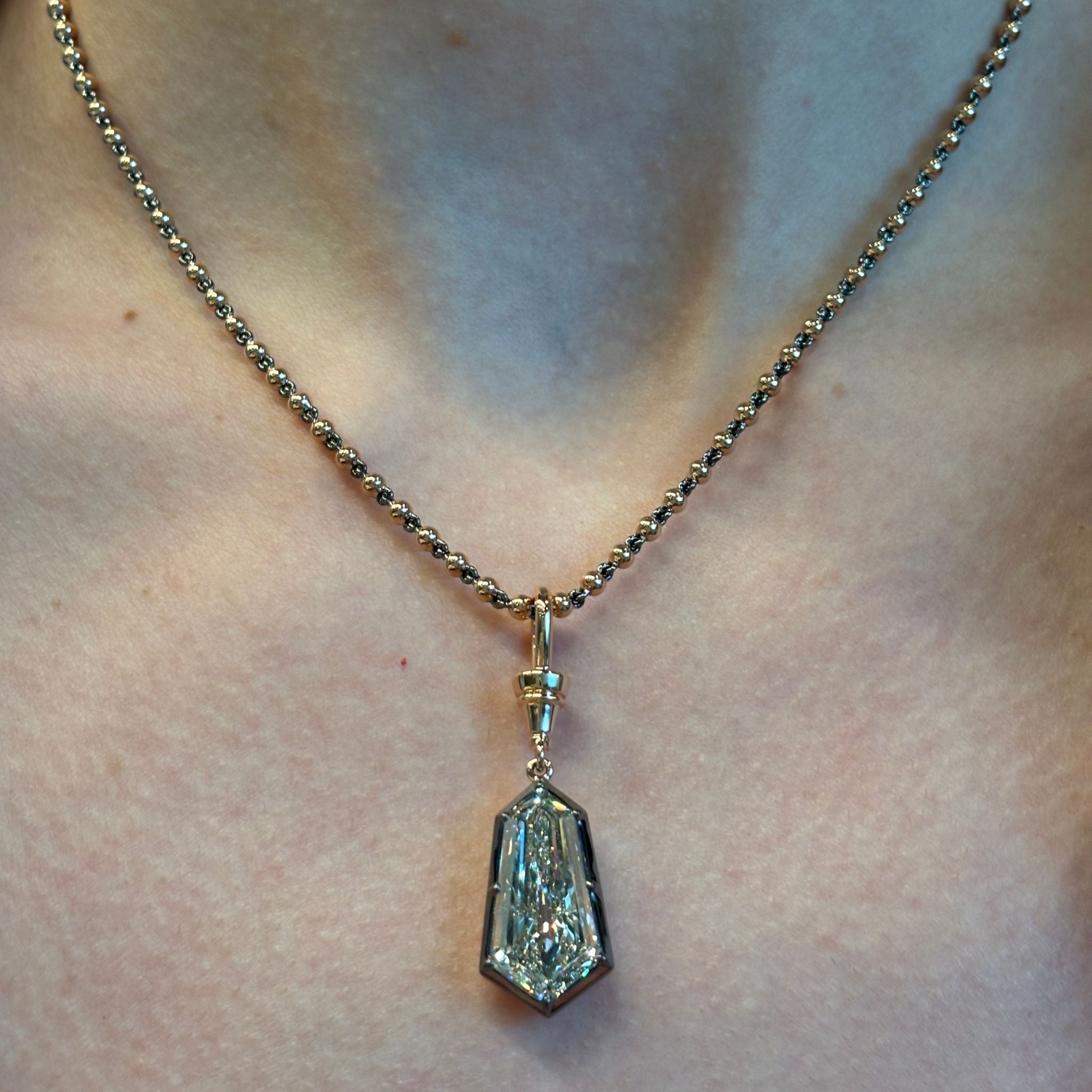 A close-up of a person wearing the Collet Set Shield Cut Diamond Necklace in Yellow Gold and Black Rhodium—a striking piece featuring a large, faceted shield-cut diamond pendant enhanced by black rhodium plating—resting at the center of their chest.