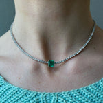 Wearing the Classic Tennis Necklace with an Asscher Cut Emerald in White Gold, featuring delicate diamonds and a central green emerald, paired with a light blue knit top.