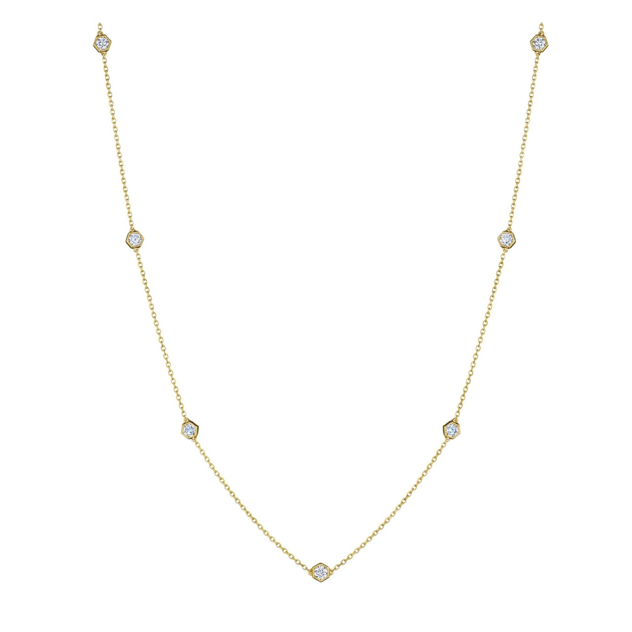 The Large Serpentine Station Necklace features seven round white diamonds, each set in a striking hexagon bezel along an 18K gold chain. This station necklace showcases a refined and modern design, elegantly displayed against a white background.