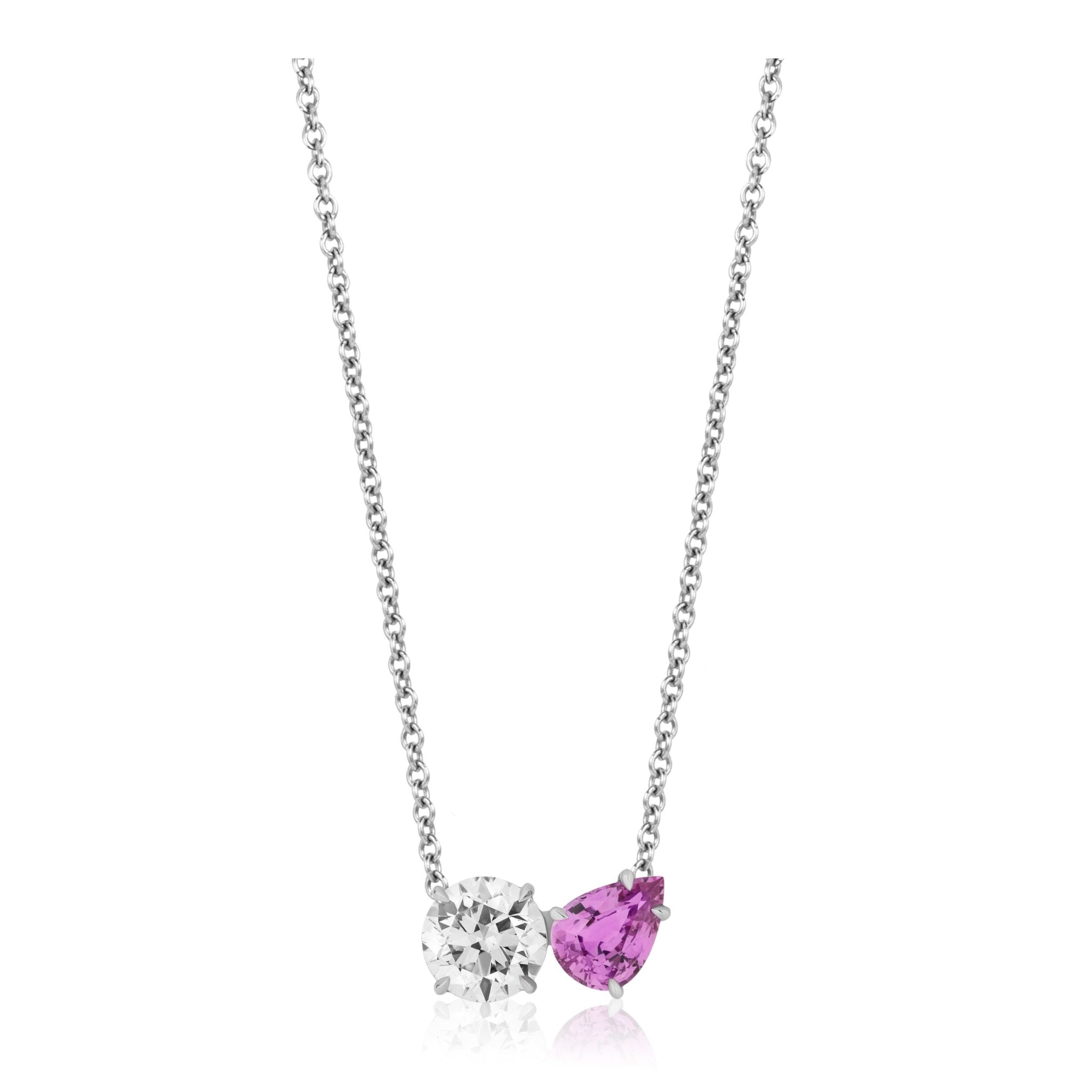 A refined white gold pendant, named the Round Diamond and Pear Shape Pink Sapphire Toi et Moi Pendant, showcases a round diamond and a pear-shaped pink sapphire set side by side on an elegant chain.