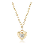 Burnish Set Heart Shape Diamond Pendant: This gold chain necklace features a shiny heart-shaped pendant with a central sparkling diamond and three small accent diamonds above it. The background is plain white.