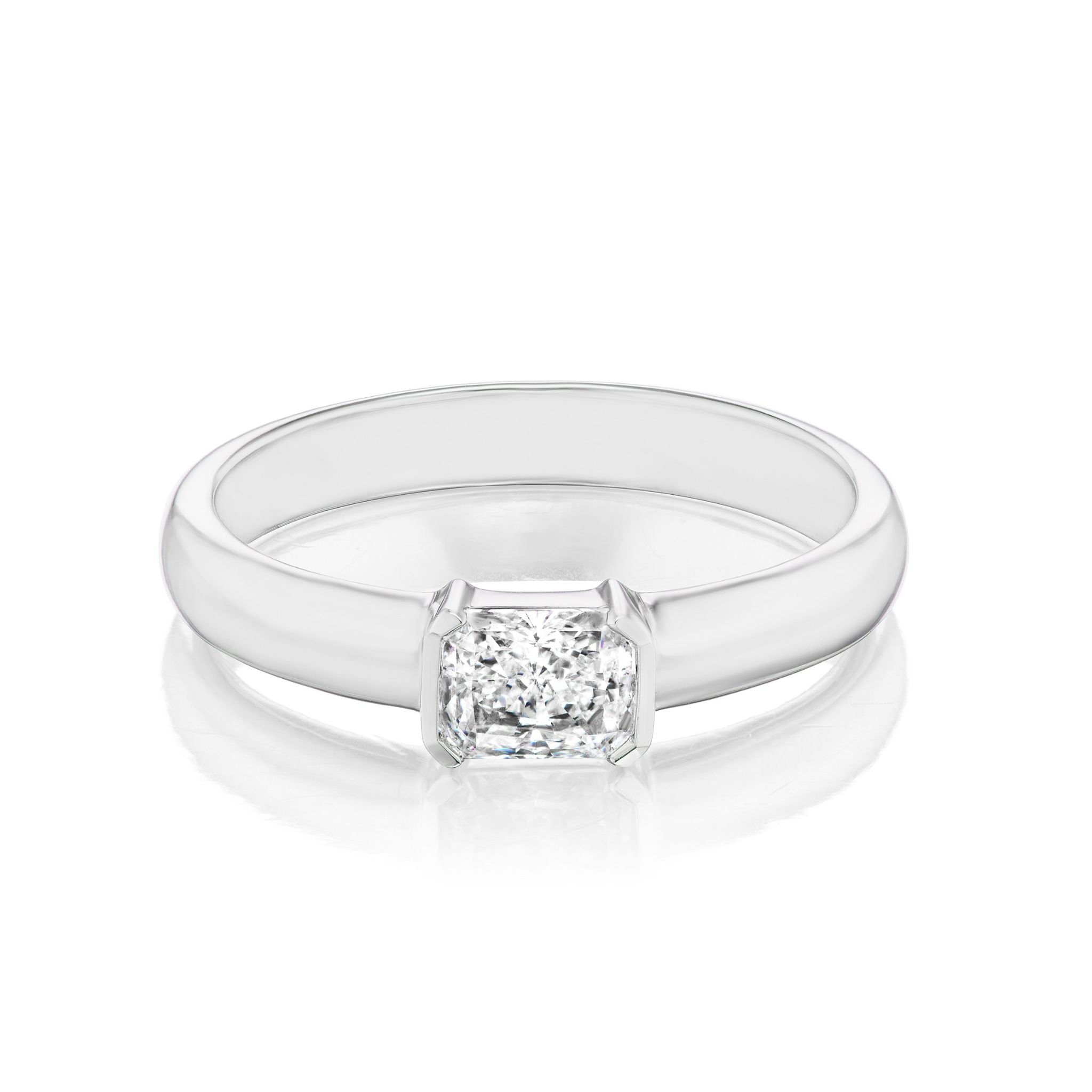 The East-West Radiant Cut Diamond Solitaire Band showcases a radiant cut diamond set sideways in 18K white gold or platinum, elegantly highlighted against a white background.