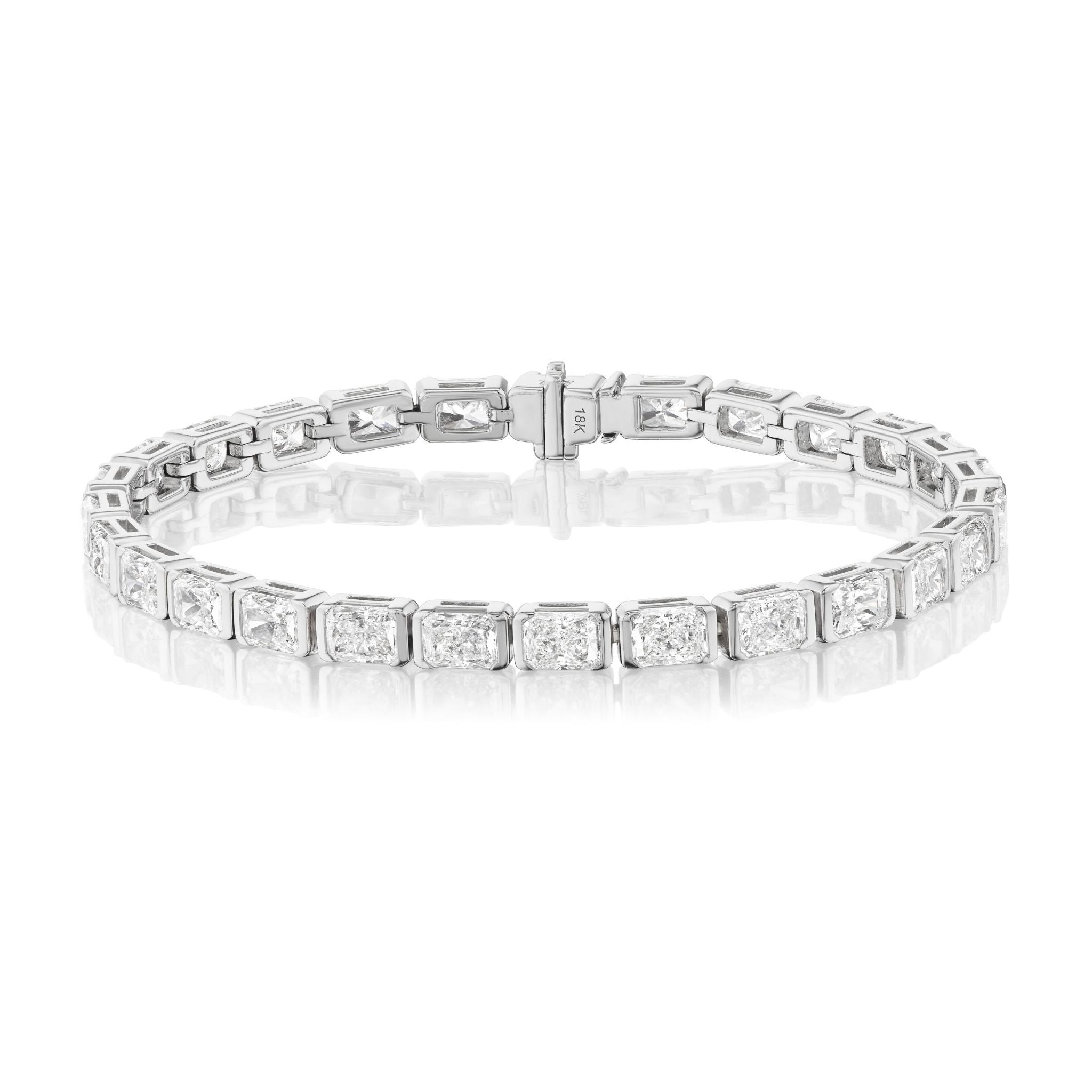 The Half-Bezel Radiant Cut Tennis Bracelet in White Gold features radiant-cut stones in sleek settings, elegantly displayed on a white reflective surface.
