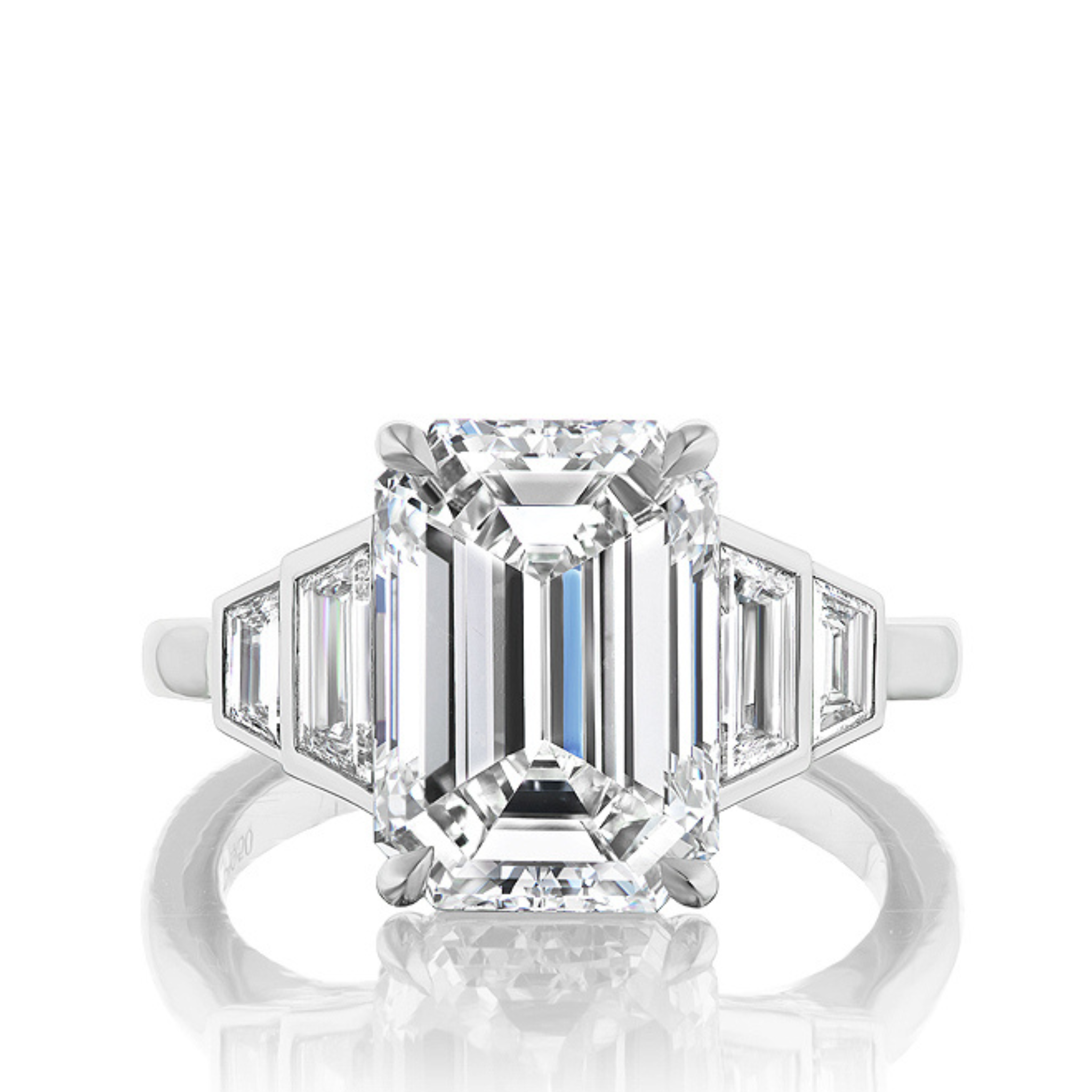 The Echo Emerald Cut Diamond Engagement Ring features a platinum band with a central emerald-cut diamond and bezel set graduating trapezoid side stones, shown against a white background.