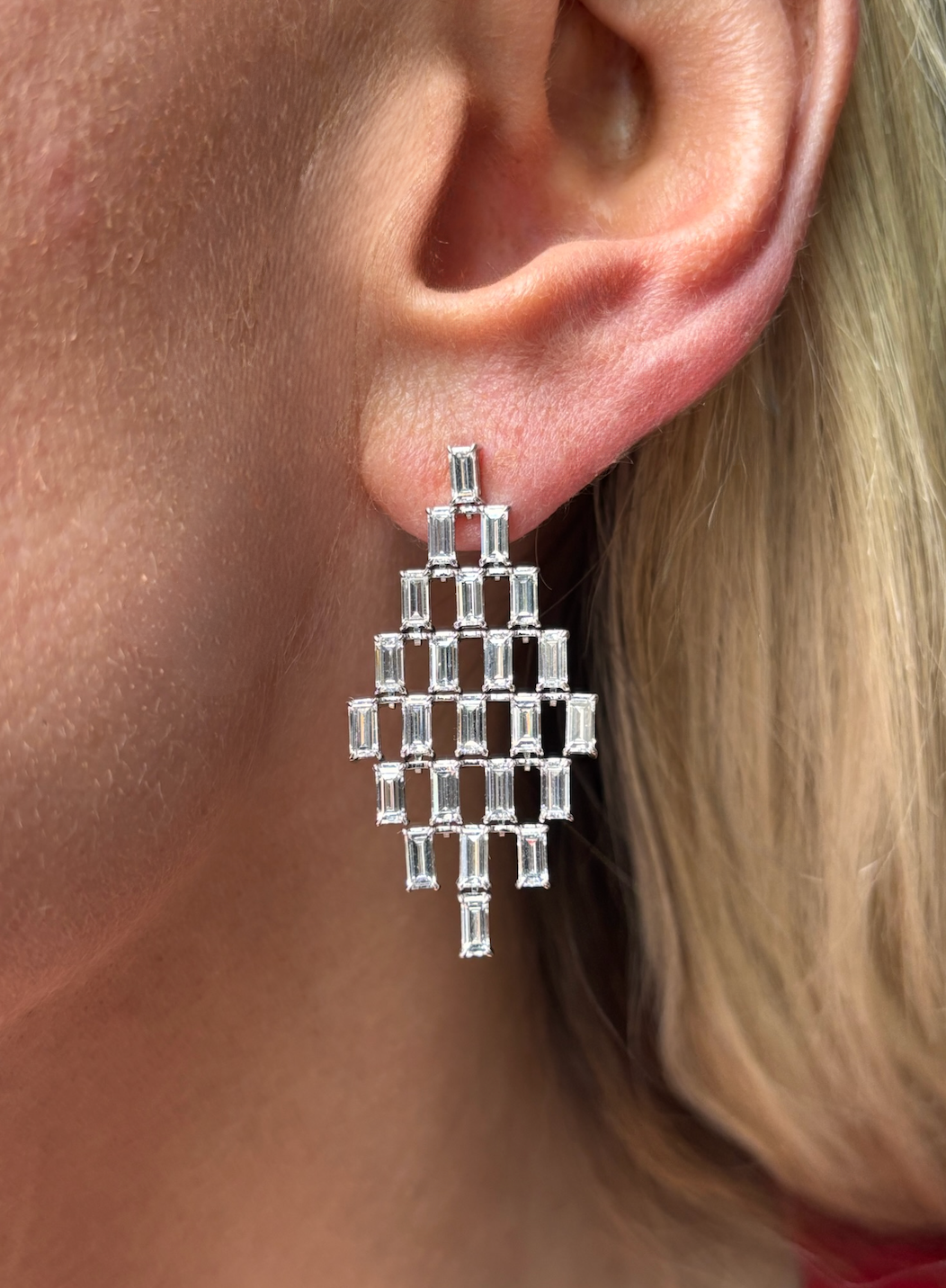 A close-up of a person with light skin and blonde hair wearing Art Deco Chandelier Earrings in white gold, featuring geometric grid-like patterns set with emerald cut diamonds.