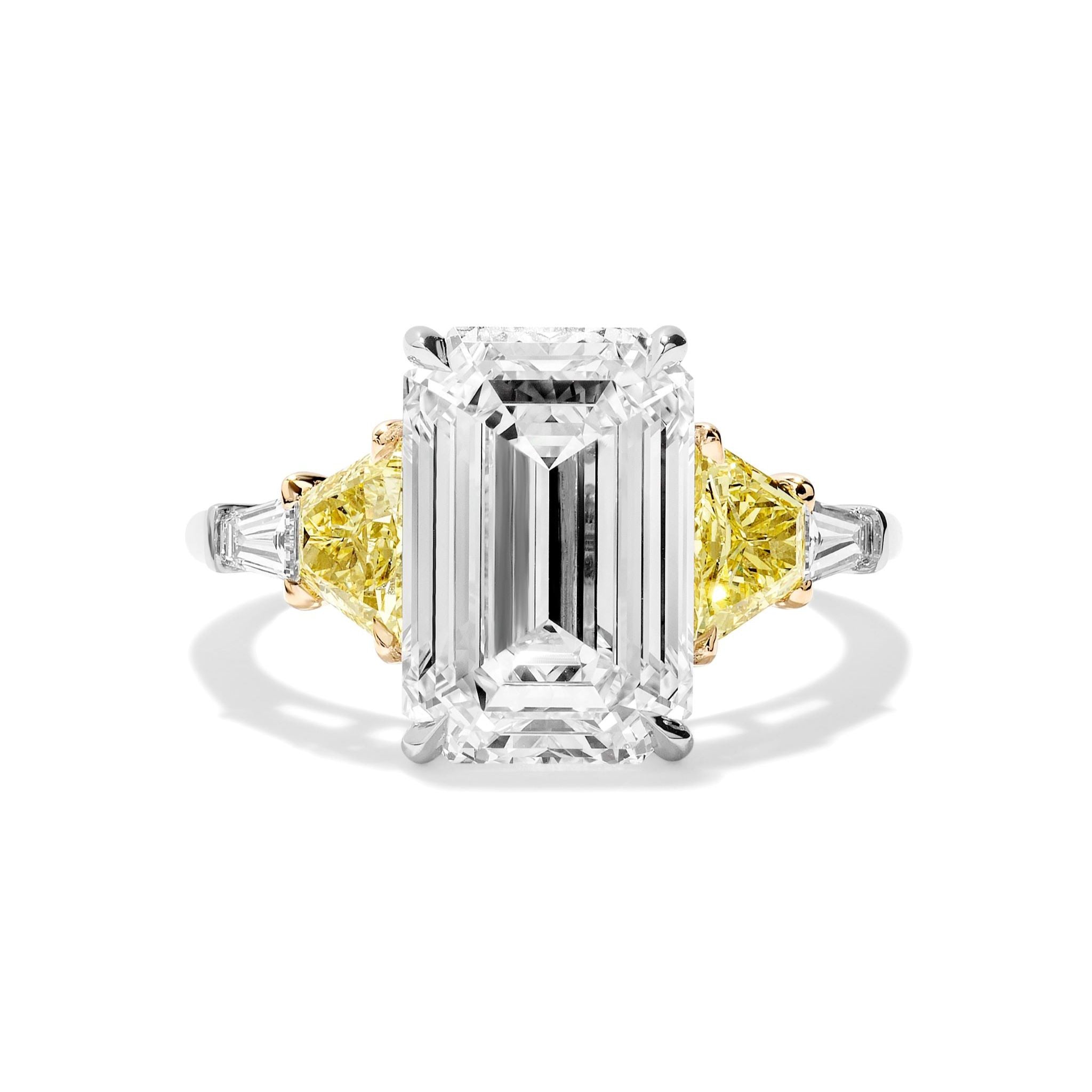 The Emerald Cut Diamond Engagement Ring features a center emerald-cut diamond, fancy yellow trapezoid side stones, and white tapered baguette accents on a white gold band.