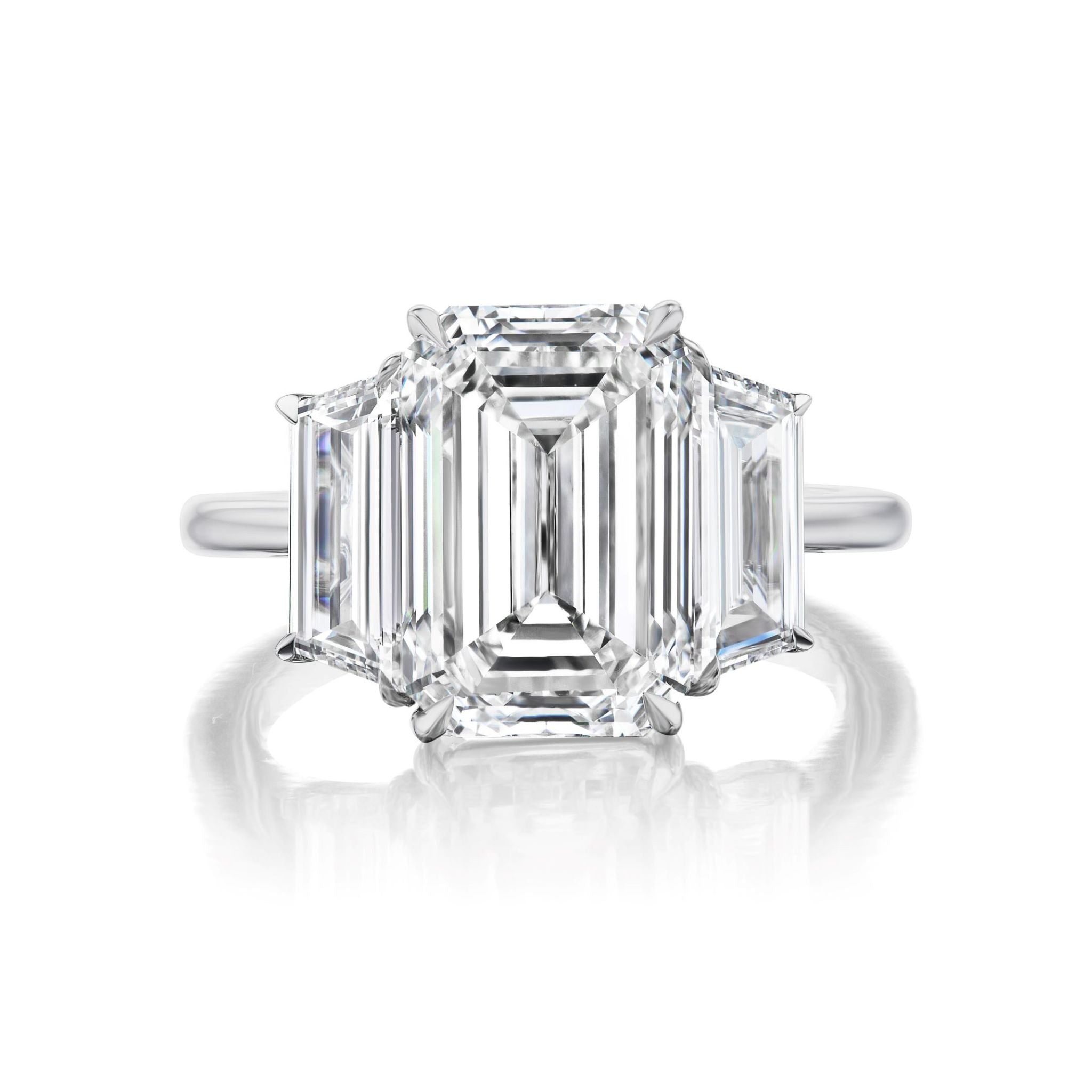 The Emerald Cut Diamond Engagement Ring features a platinum band with a large emerald-cut center diamond accented by trapezoid side stones for a sleek, modern look.