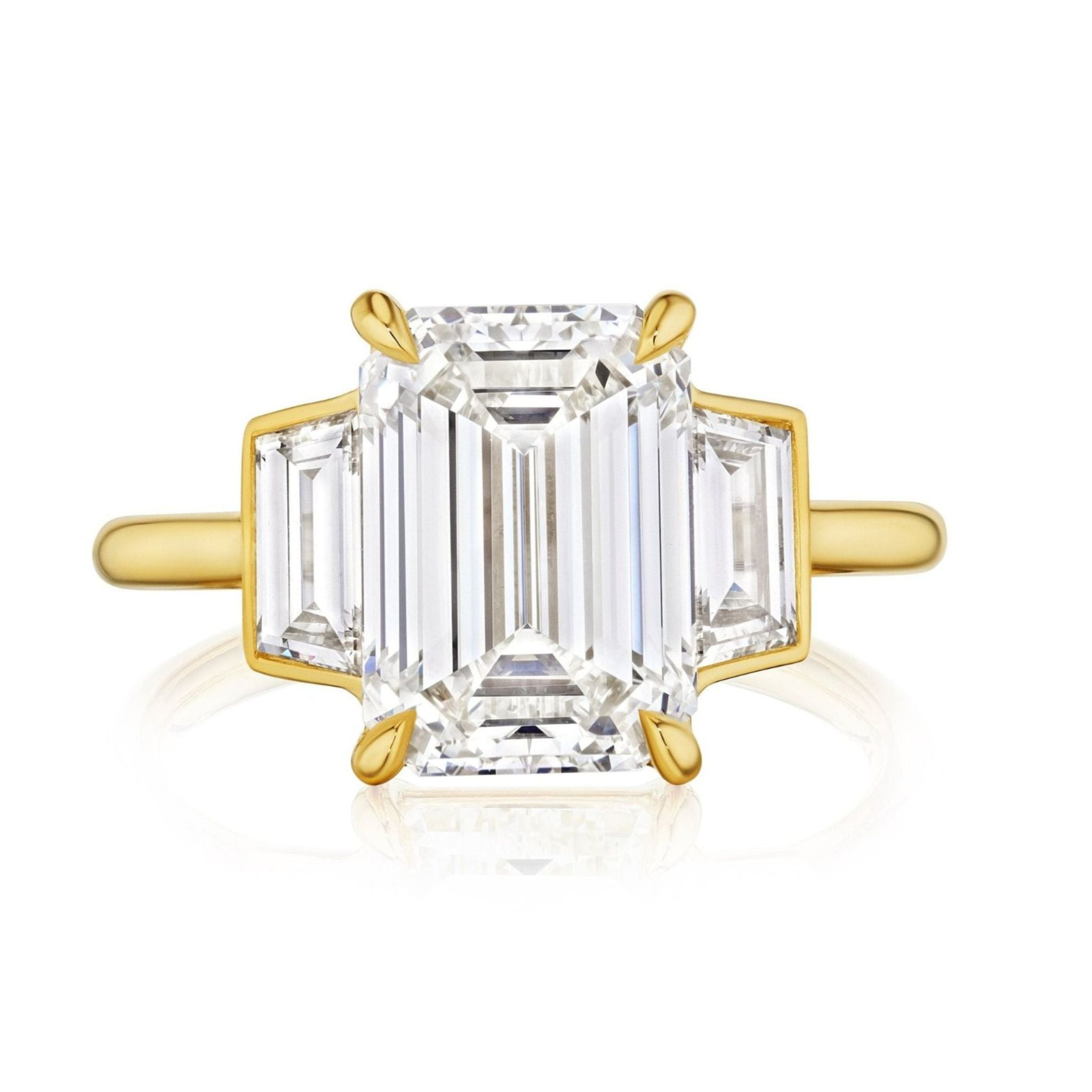 The Emerald Cut Diamond Engagement Ring with Trapezoid Side Stones features a large center emerald cut diamond and two trapezoid diamonds, all set in an elegant 18k yellow gold band.