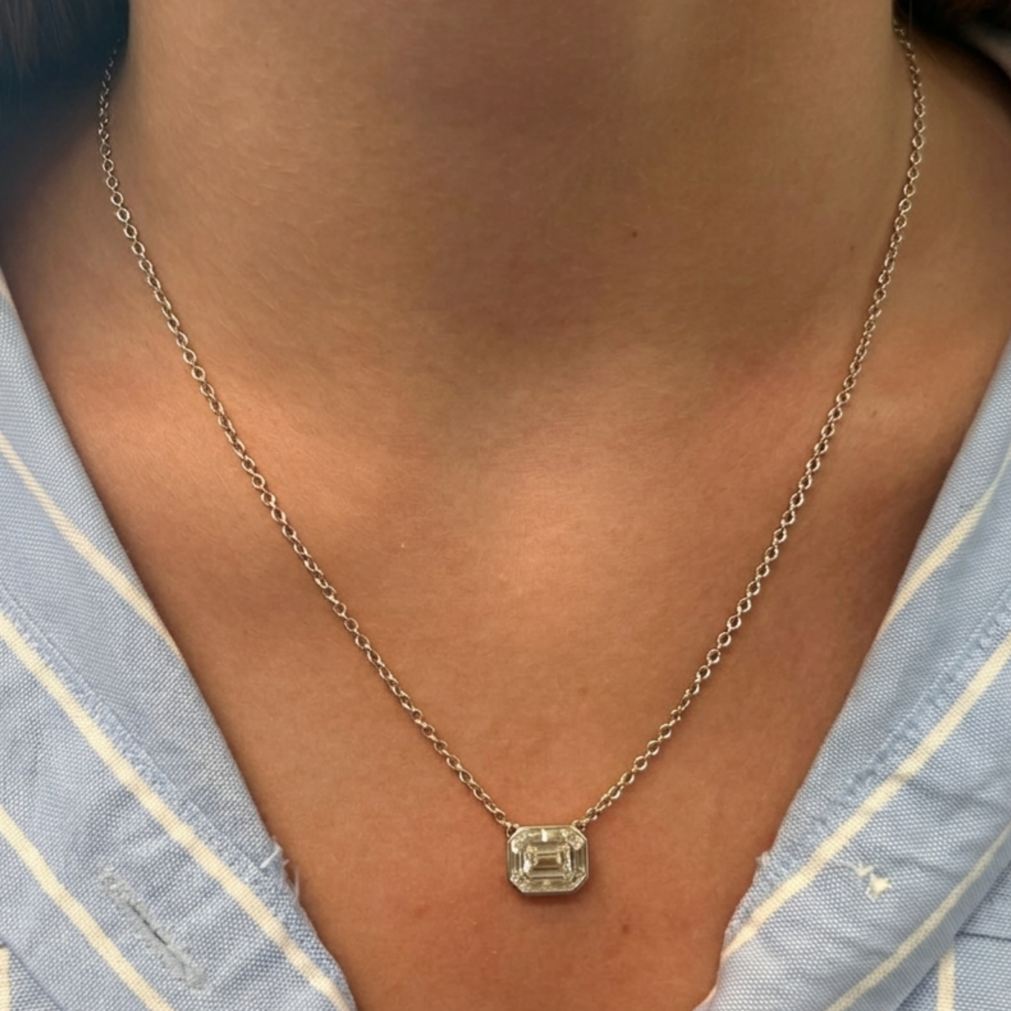 A close-up of a person wearing the Emerald Cut Mosaic Pendant in white gold, paired with a light blue and white striped shirt.