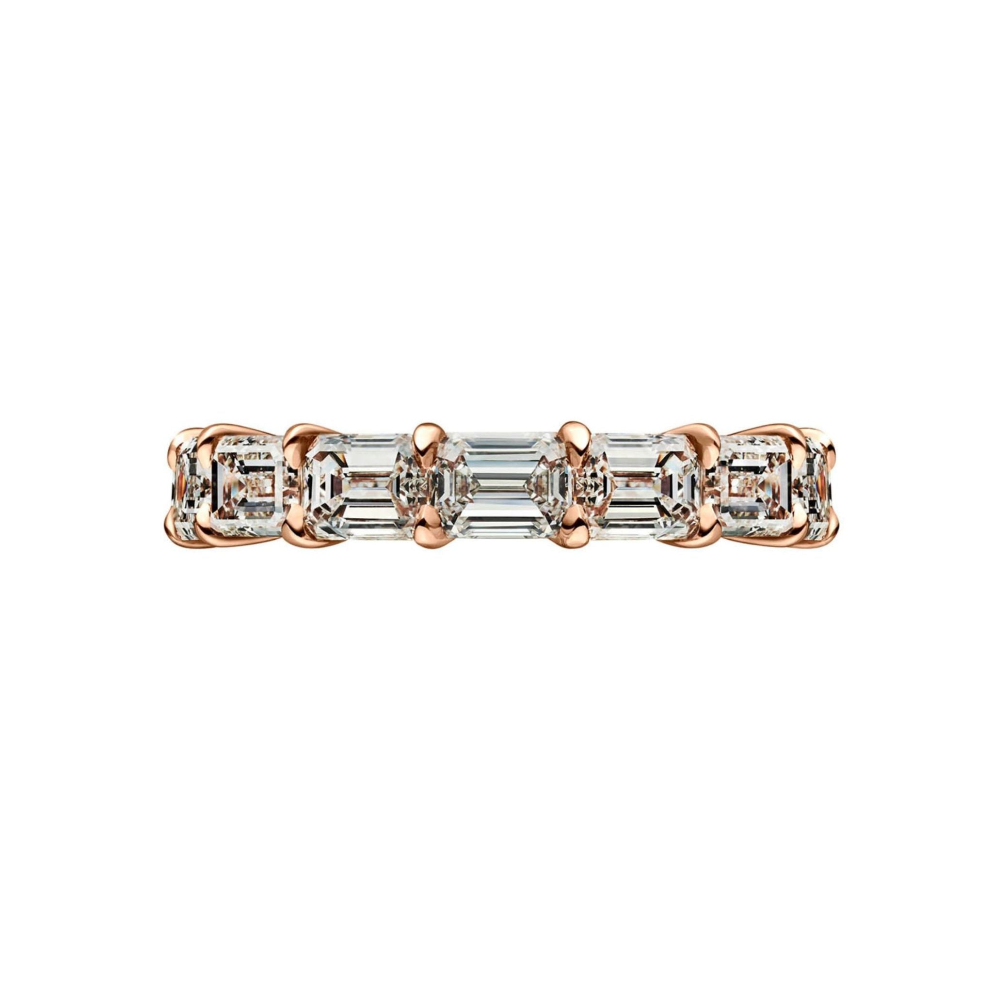 The East-West Emerald Cut Diamond Eternity Band is shown on a white background, featuring a row of rectangular, emerald-cut diamonds with D-E color and VVS1 clarity set horizontally across the gold band.