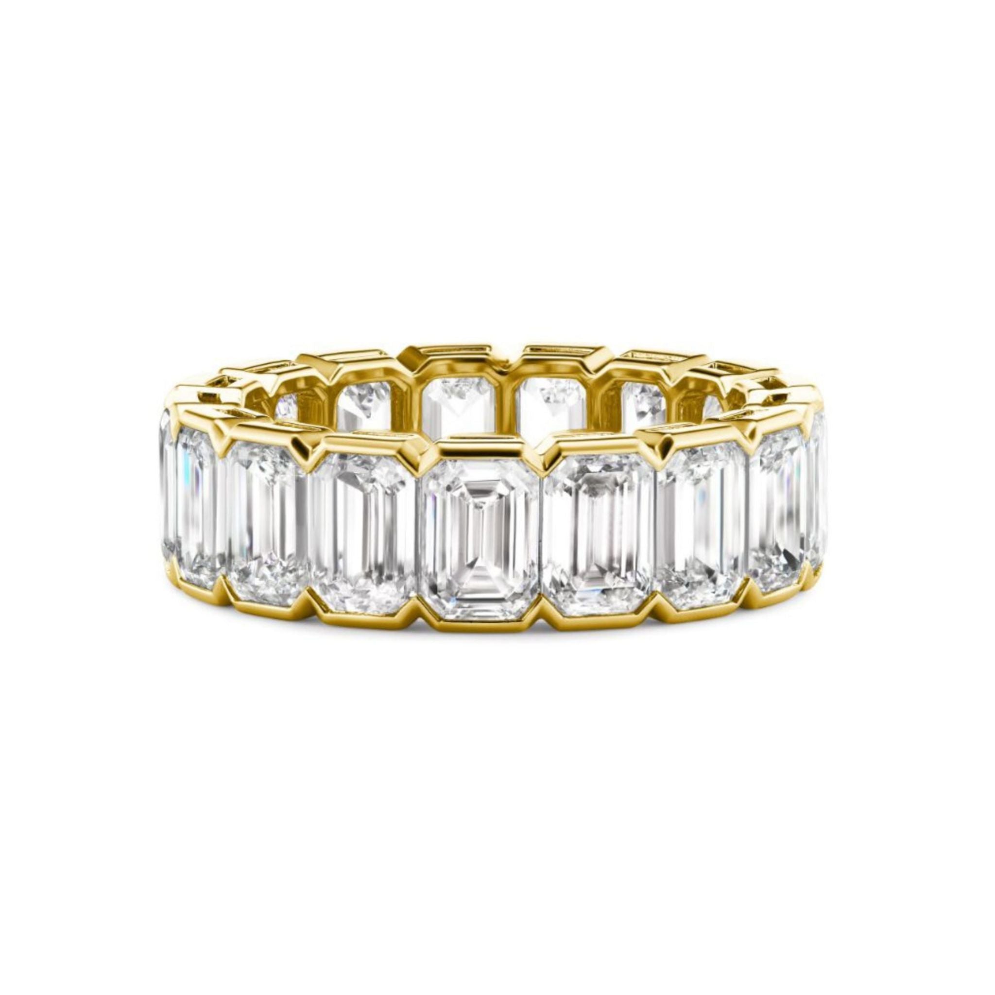 The Half Bezel Emerald Cut Diamond Eternity Band features a gold setting with large emerald-cut diamonds encircling the entire band, shown against a white background—an elegant choice for bridal bands or celebration rings.