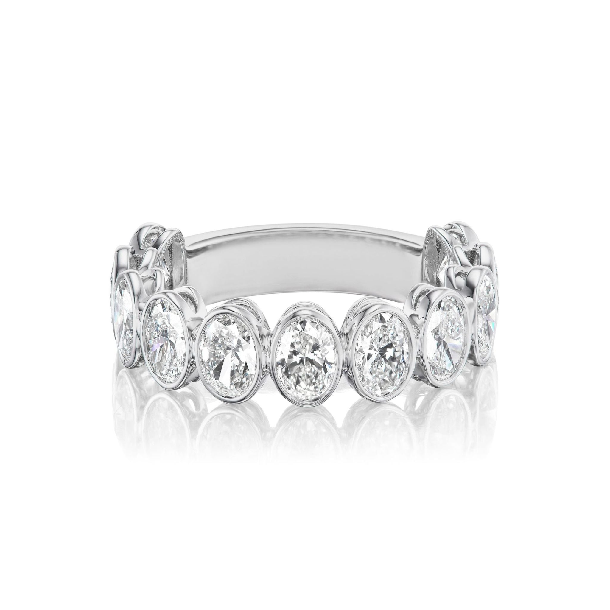 An Oval Bezel Set Diamond Half Eternity Band is displayed on a white reflective surface, featuring a row of oval, bezel-set diamonds around the band.
