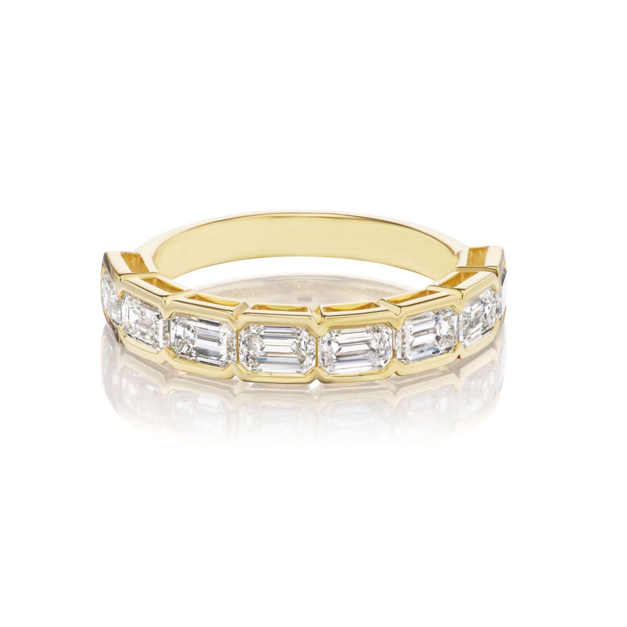 The East-West Bracket Bezel Emerald Cut Diamond Half Eternity Band showcases a row of rectangular emerald-cut diamonds set in an elegant east-west orientation, beautifully displayed on a reflective white surface—an ideal choice for those seeking refined bridal rings or sophisticated celebration rings.