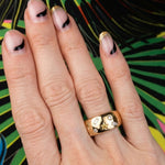 A hand displays the Yellow Diamond Celestial Cigar Band, an elegant 18k yellow gold ring showcasing star and diamond motifs. The nails feature a French manicure with black tips and gold glitter accents, set against a colorful abstract background.