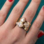 A hand with red nail polish wears three Bezel Set Mixed Shape Diamond Thick Bands in Yellow Gold, each featuring uniquely shaped clear diamonds, against a teal fabric background.