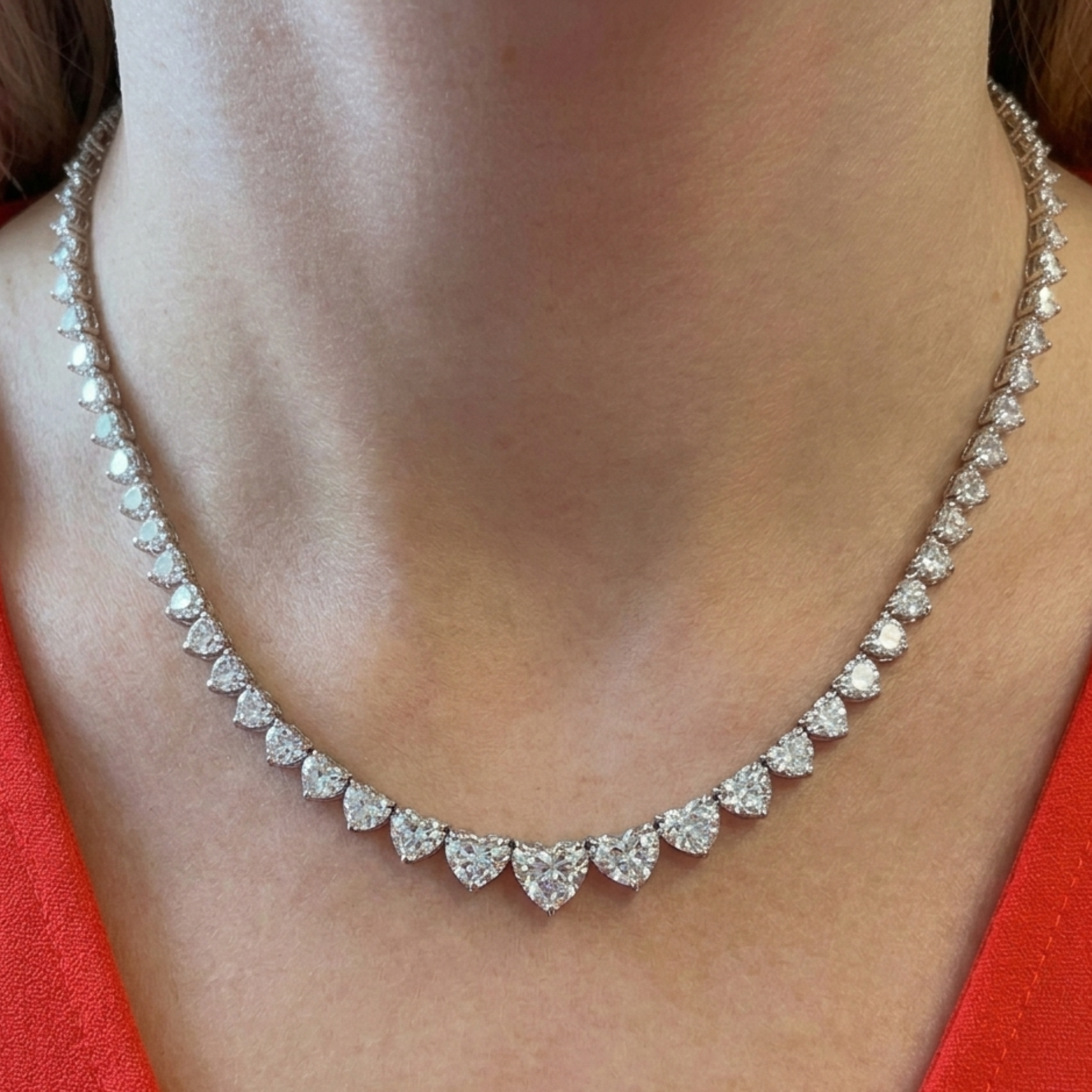 A close-up of a woman's neck showcases the Graduated Heart Diamond Tennis Necklace in White Gold, paired with a red top.