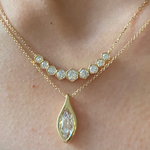 Two delicate 18k gold necklaces adorn the neck: a Bezel Set Hexagon Necklace with Graduated Brilliant Diamonds and a diamond necklace with a gold marquise-shaped pendant featuring a single sparkling stone.