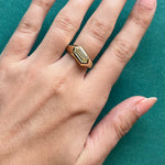 A hand with neatly manicured nails wears the Chunky Hexagonal Ring in Yellow Gold with Fancy Light Yellow Diamond, resting on a green surface.