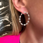 A close-up of a person with blonde hair in a bright pink top, wearing Light Mixed Shape Diamond Hoops—large 18K gold earrings adorned with sparkling G-H color mixed shape diamonds.