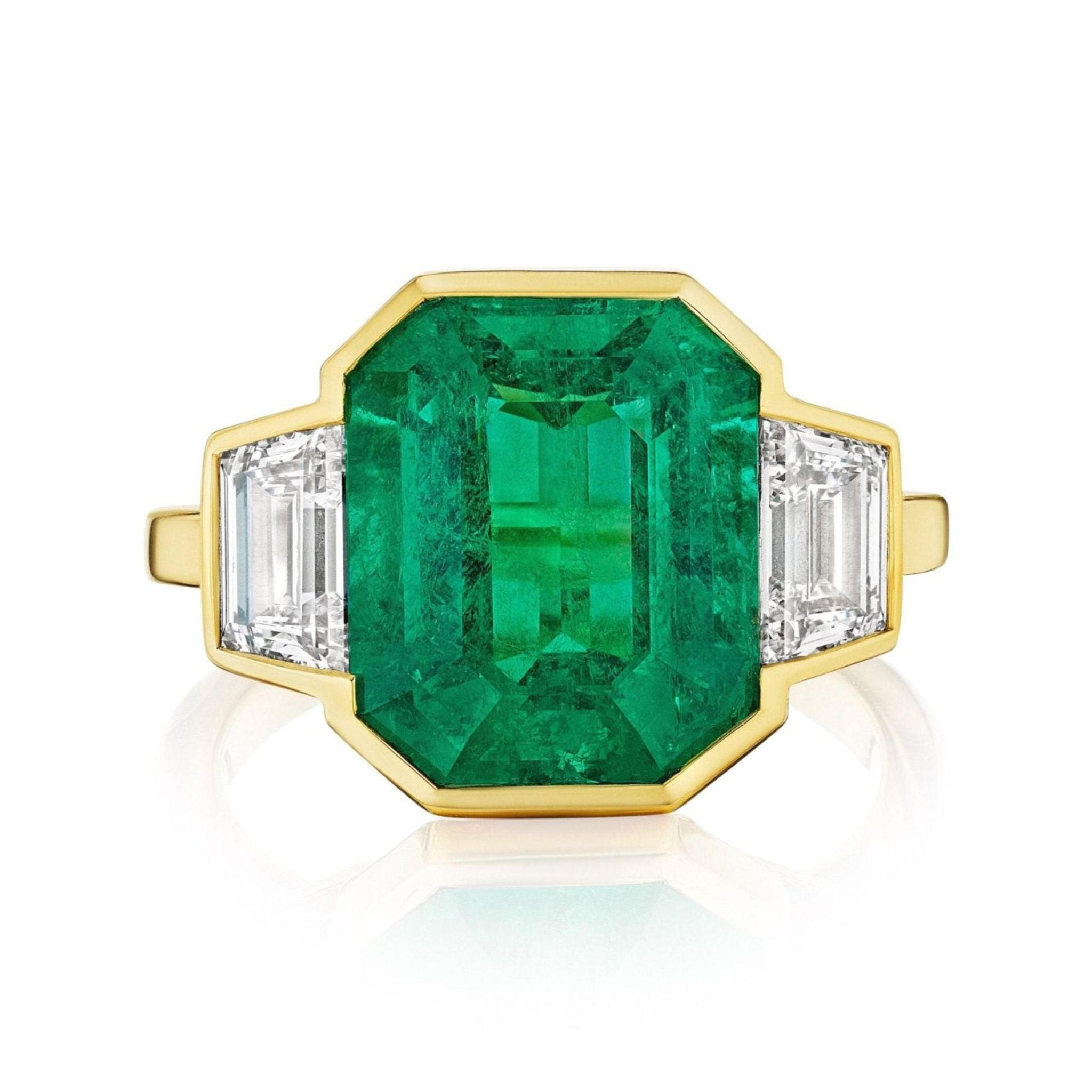 The Half Bezel Set Emerald Cut Emerald Engagement Ring features an emerald center, trapezoid diamond side stones, and is crafted in luxurious 18k yellow gold.