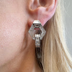 Close-up of a woman's ear wearing Chrysler Interlocking Hexagon Earrings with Baguette Diamonds in 18K white gold, featuring two hexagonal shapes set with baguette diamonds. Her blonde hair is partially visible.
