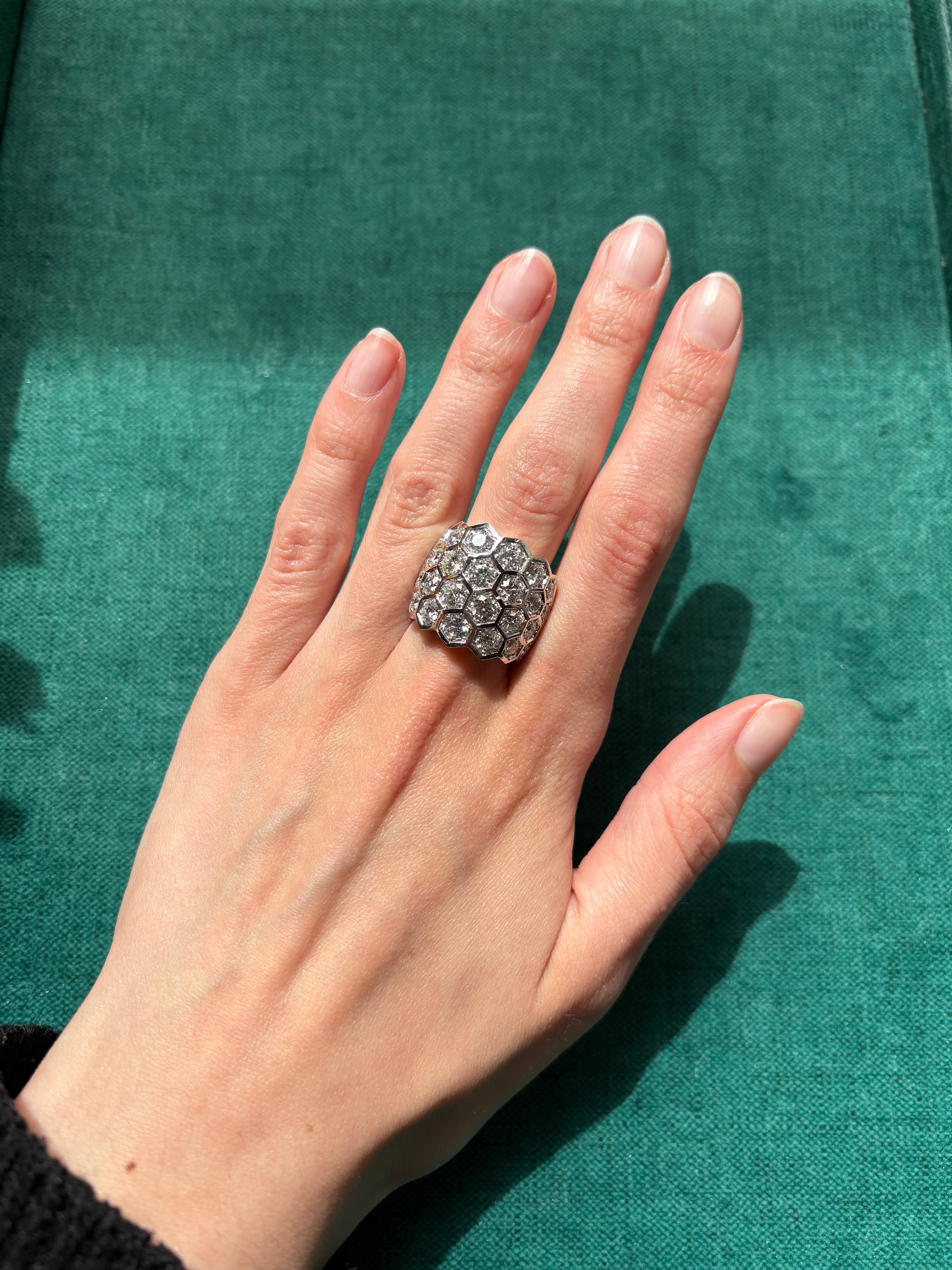 A hand with neatly manicured nails displays the Hexagon Bezel Set Multi-Tier Chunky Band with round diamonds in yellow gold, set against a green textured background.