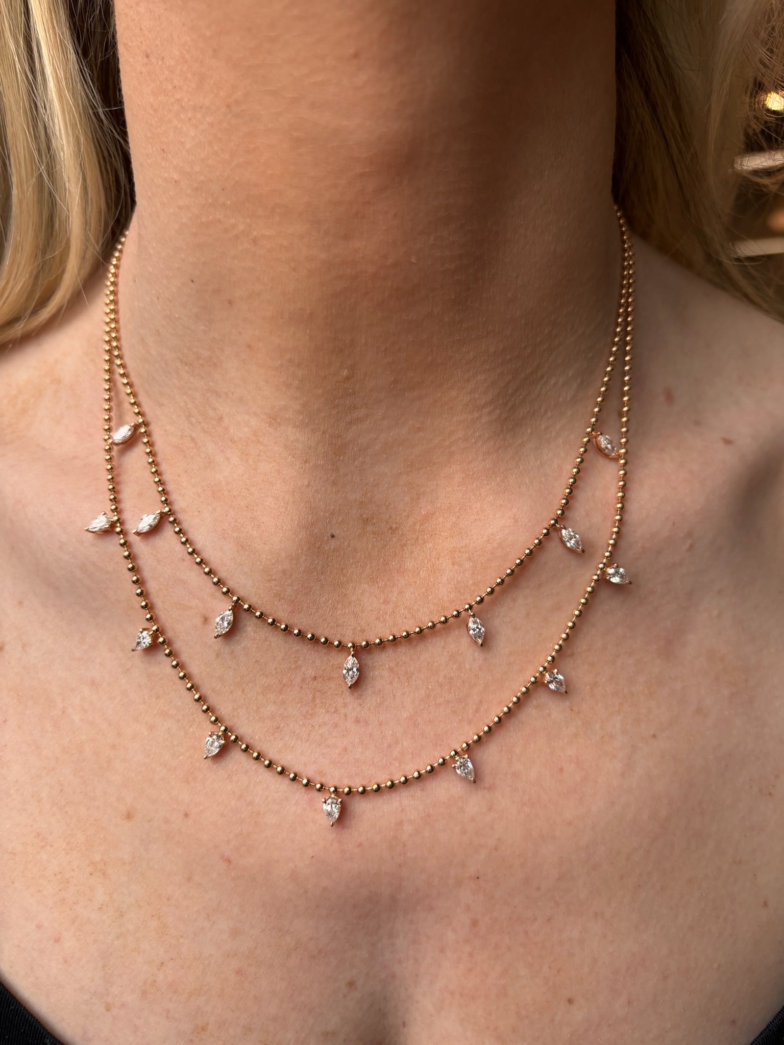 A close-up of a person’s neck wearing the Spike Ball Chain Necklace in Yellow Gold with marquise pink sapphires, featuring double-layered chains with sparkling stones, paired with a black top.