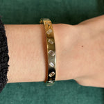 An elegant Alternating Burnish Set Emerald Cut Diamond Bangle in Yellow Gold adorns a wrist against green fabric, with part of a black sleeve visible.